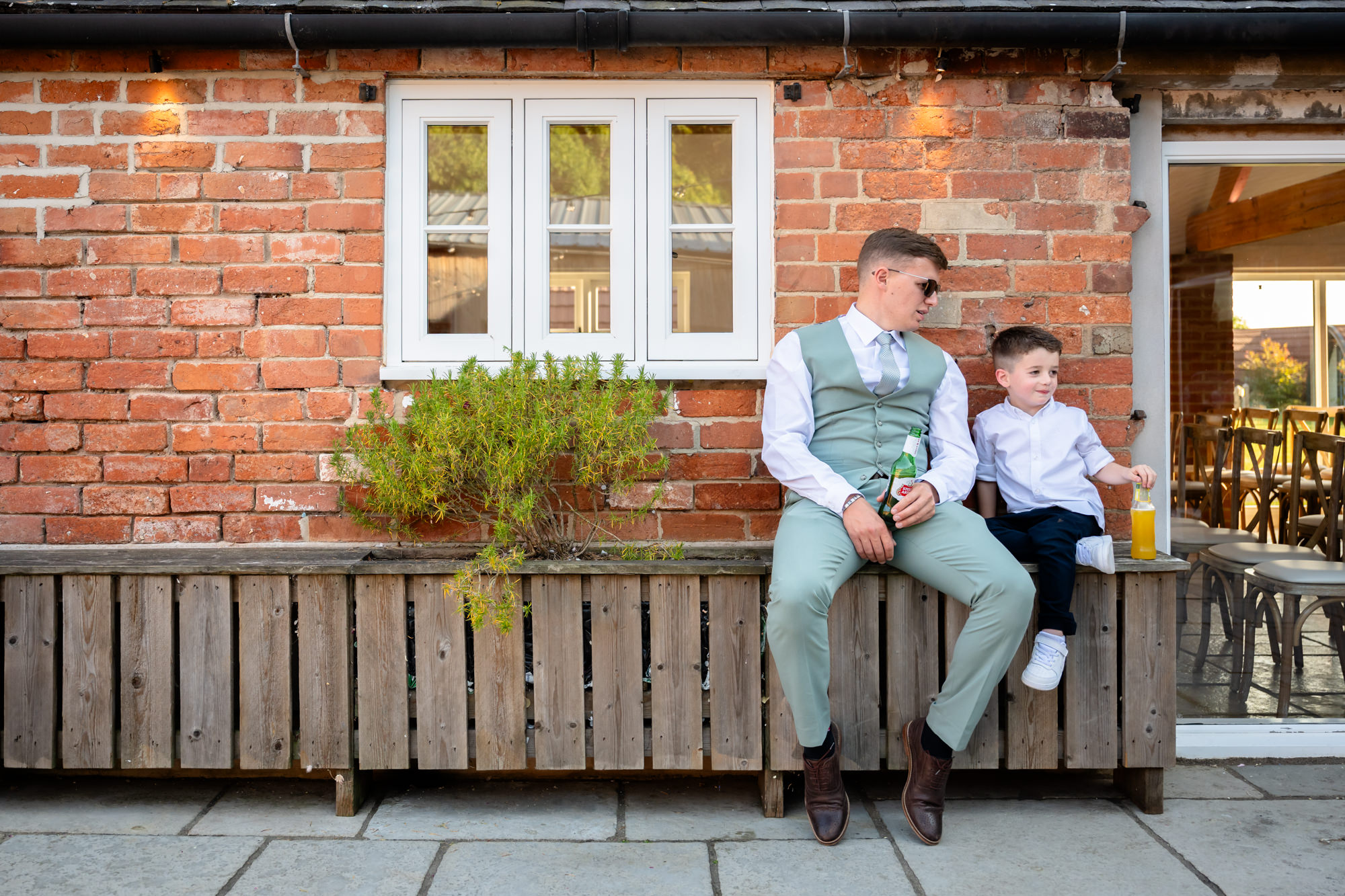 A man and a young boy are sitting together outside on a bench at a wedding at Hanbury Barns.