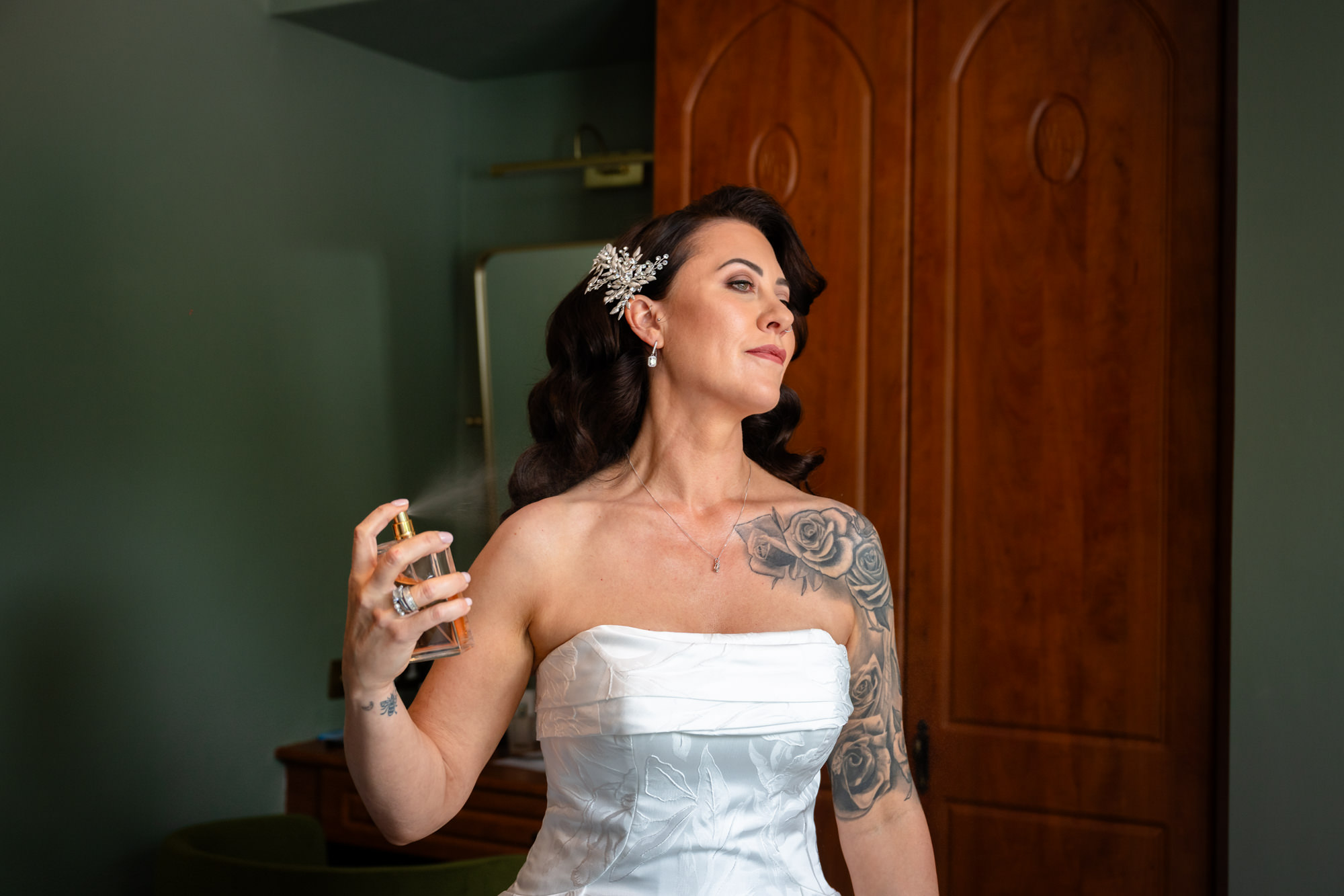 A smiling bride in a white strapless dress applies a spritz of perfume to her neck at Springbank Manor.
