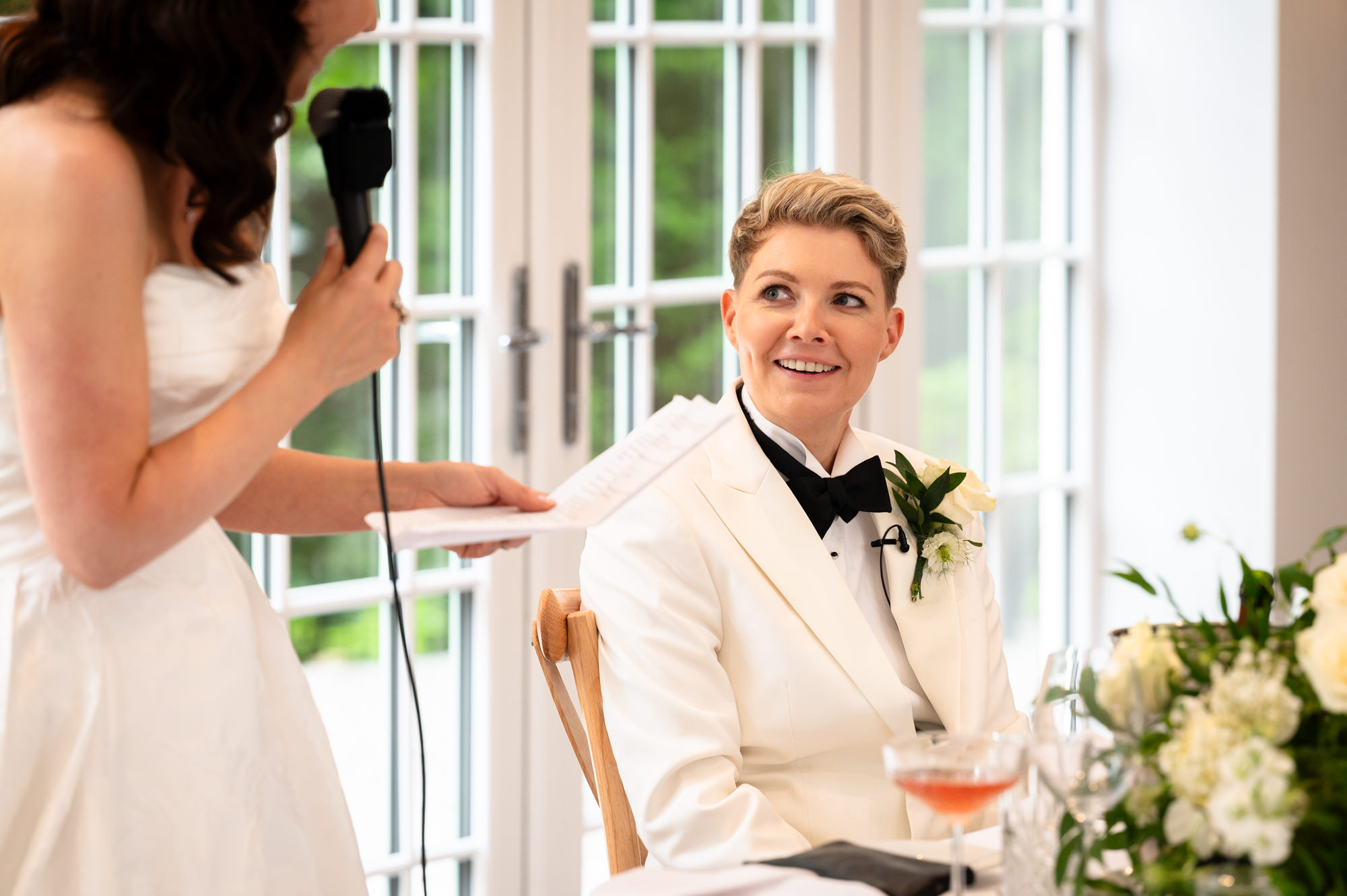 A photo from the wedding at Springbank Manor of the two brides at a table, with one of them smiling and looking at the other.