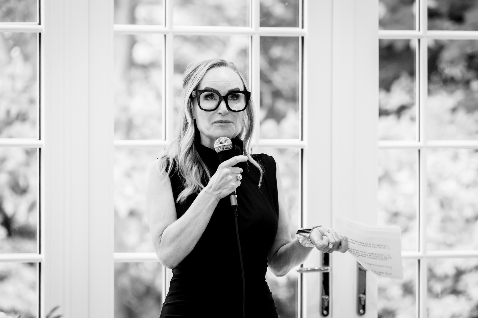 A black and white photo of a woman in a black shirt giving a speech and holding a microphone at Springbank Manor.