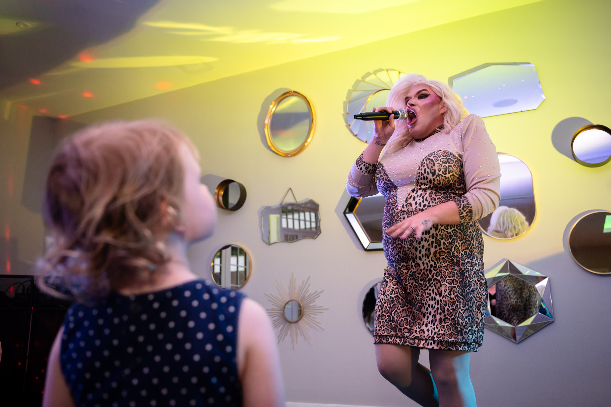 A drag queen performs on a stage while young girl looks on at Springbank Manor.