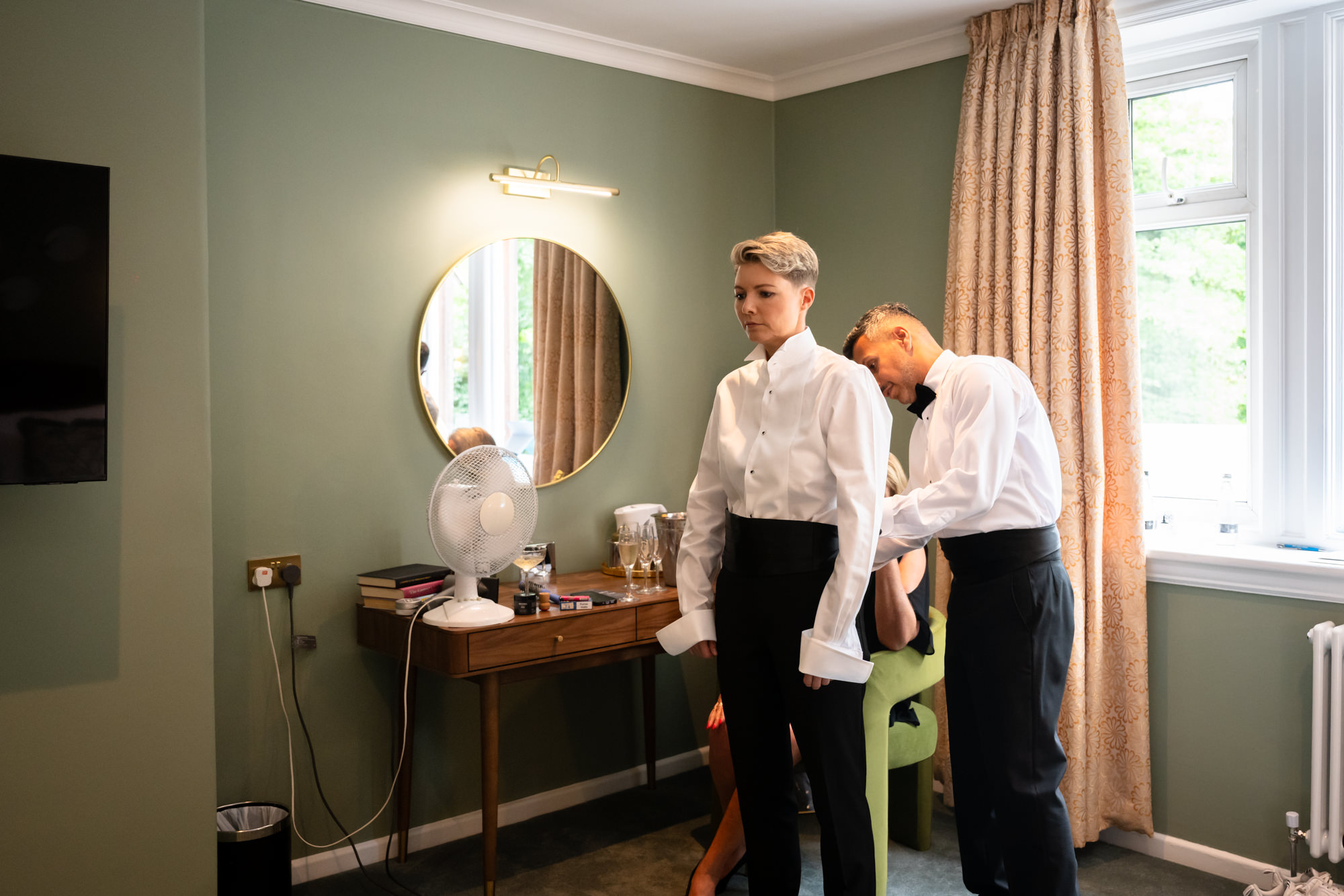 A man adjusts the cummberbunds on the white tuxedo jacket of one of the brides at the Springbank Manor wedding.