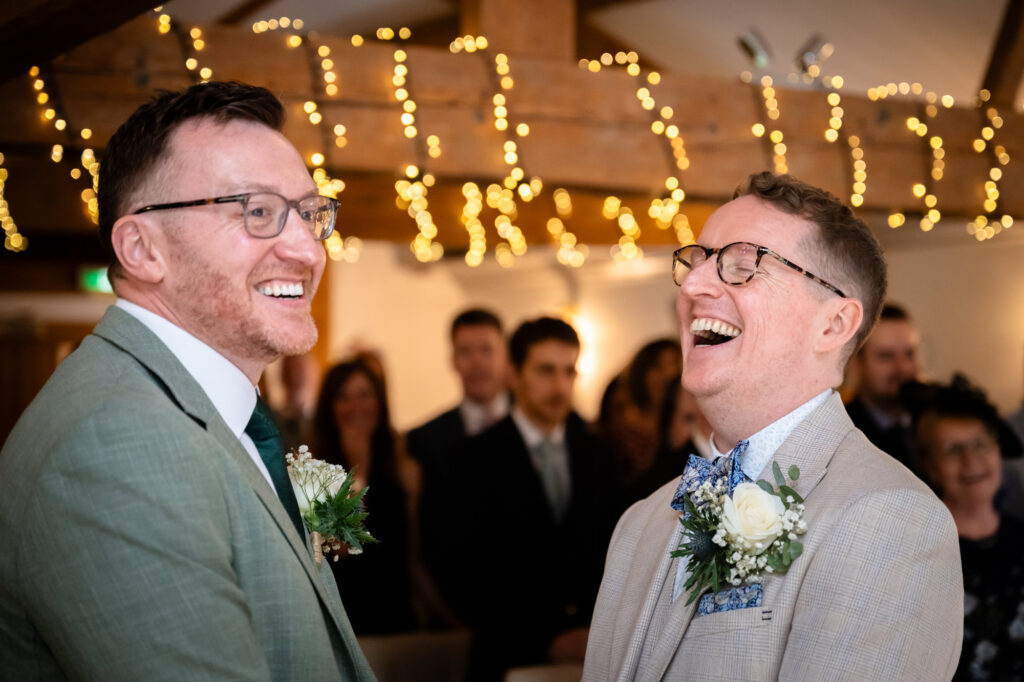 A close-up portrait of the grooms during their ceremony, smiling at each other with twinkle lights blurred in the background.