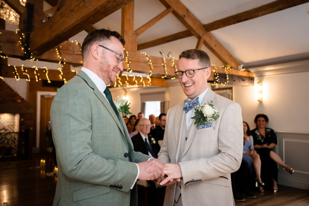 The grooms stand facing each other during the ceremony, with one holding the other's hand as they exchange vows.