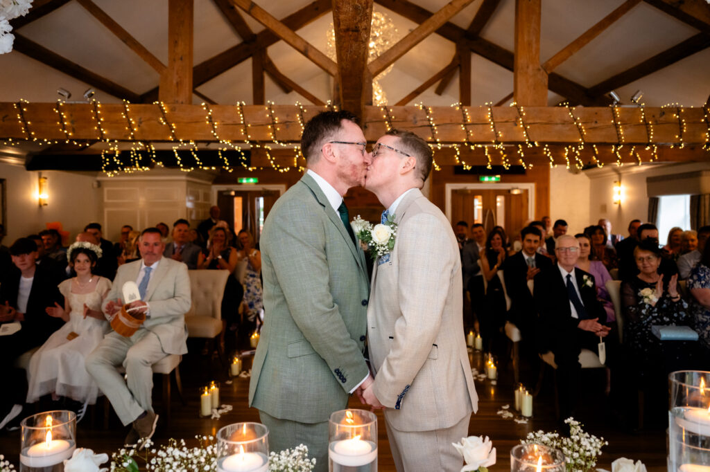 The grooms face each other, leaning in for a kiss during the ceremony.