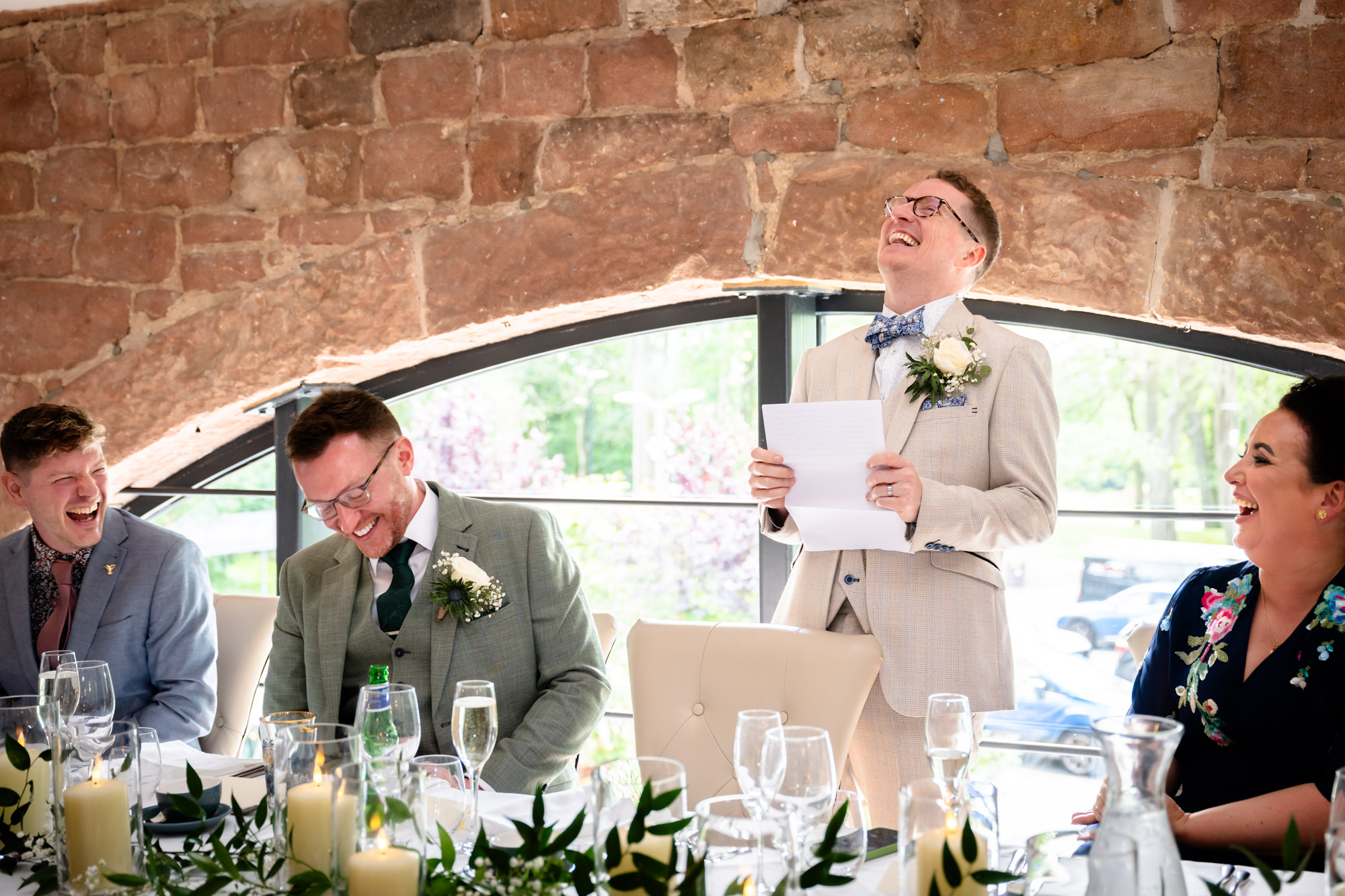 The groom in a beige suit stands and gives a speech during the wedding breakfast at Allerton Manor.