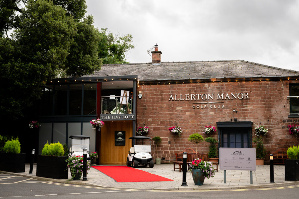 The front of the Allerton Manor venue, a brick building with a red carpet leading to the entrance and a sign for The Hay Loft.