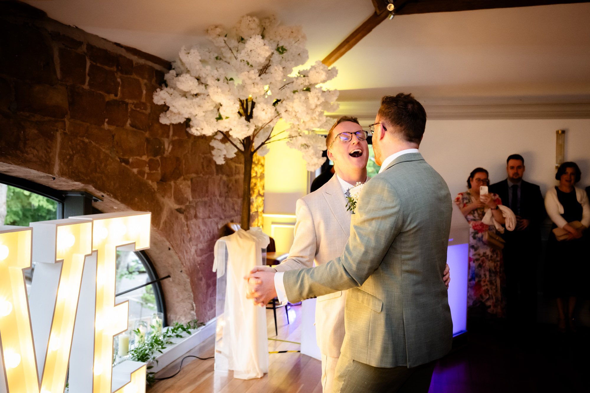 The grooms smile while holding each other, dancing together during their first dance.