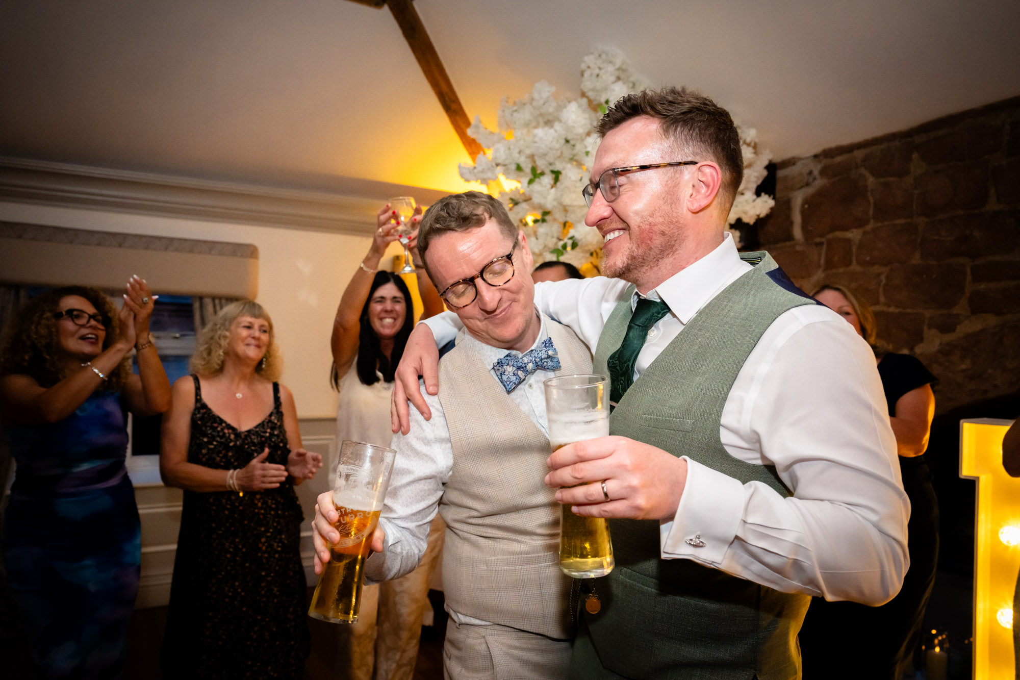 The grooms are dancing together, with a beer in their hand.