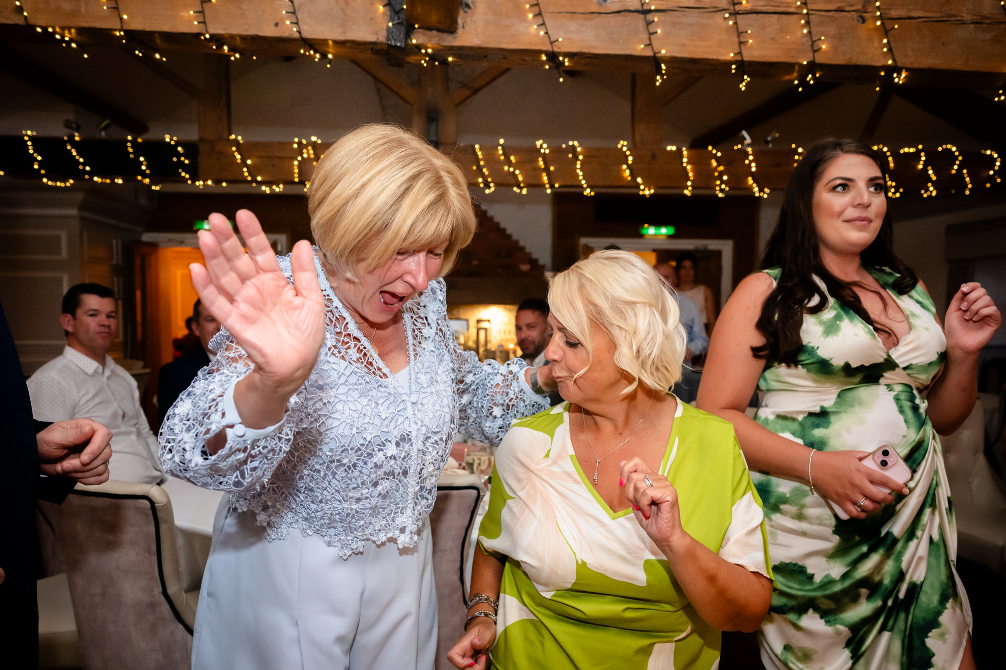 Two women are dancing together during the party, one in a white jacket and the other in a light green top.