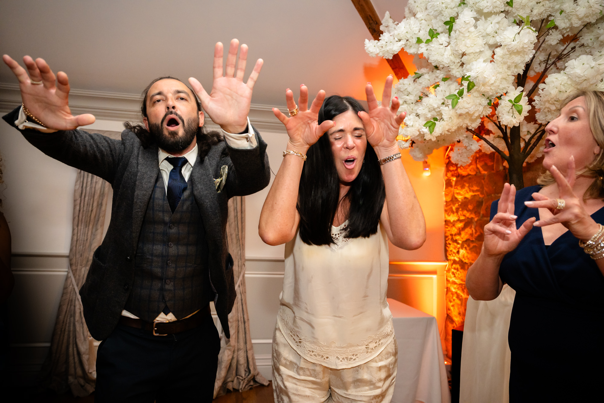 A group of people are dancing, with one man in a suit raising his hands high in the air and laughing.