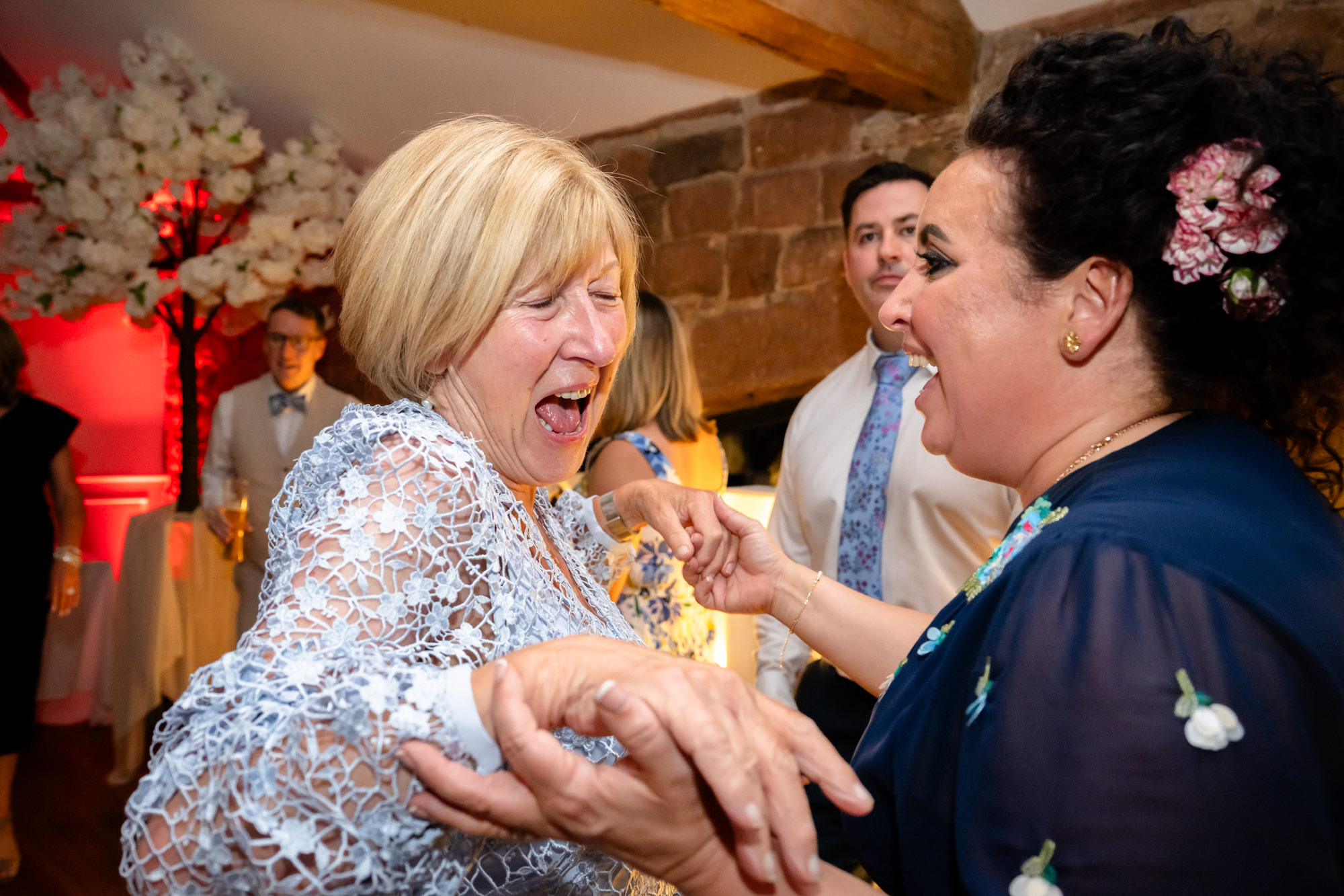 The groom's mother dances with a woman with a large updo during the party.