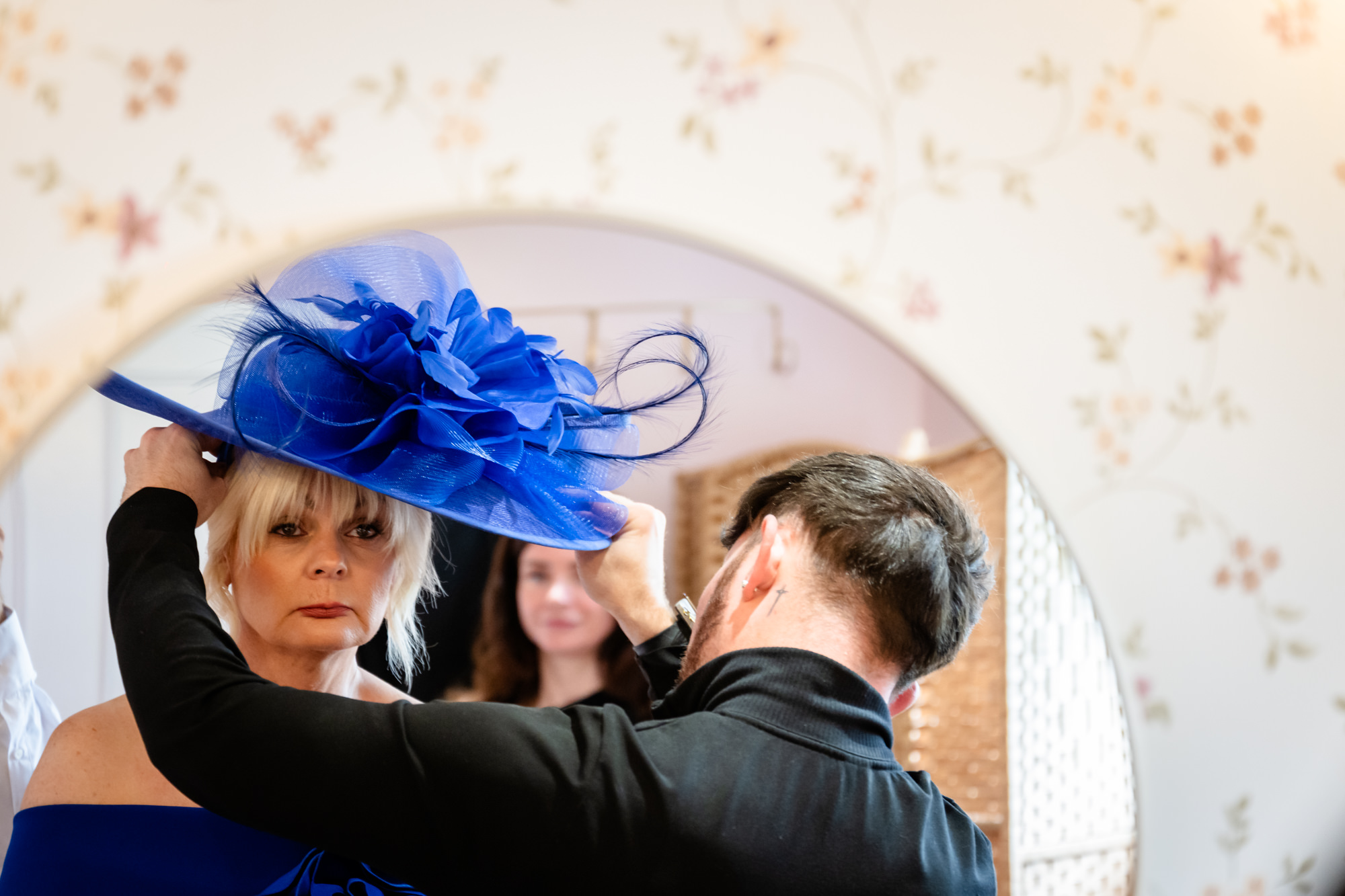 A wedding day at Hanbury Barns portrait of the bride's mother adjusting her bright blue fascinator before the ceremony.