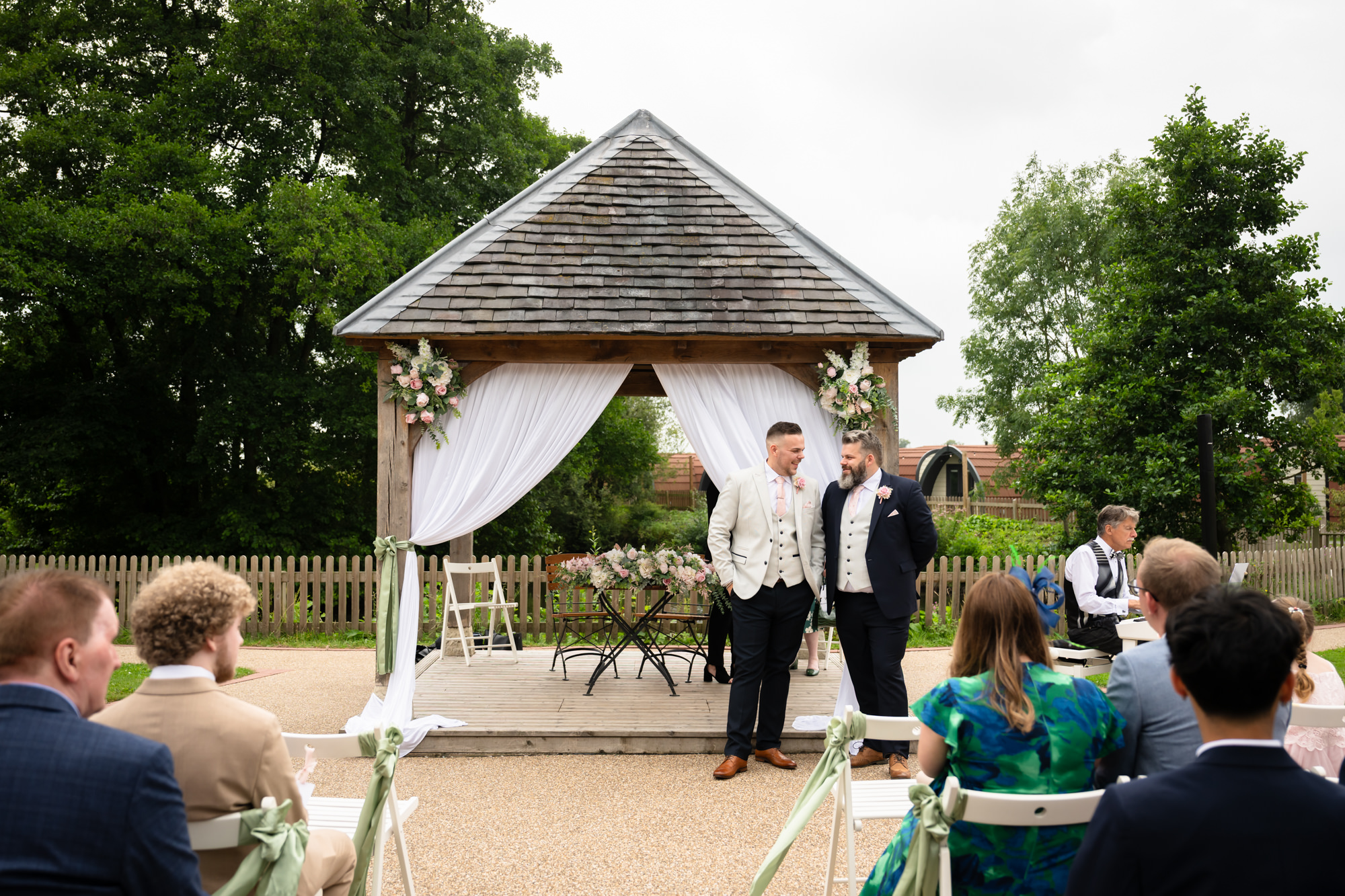 The groom and his best man standing with the registrar in the outdoor gazebo area at Hanbury Barns during the wedding ceremony.