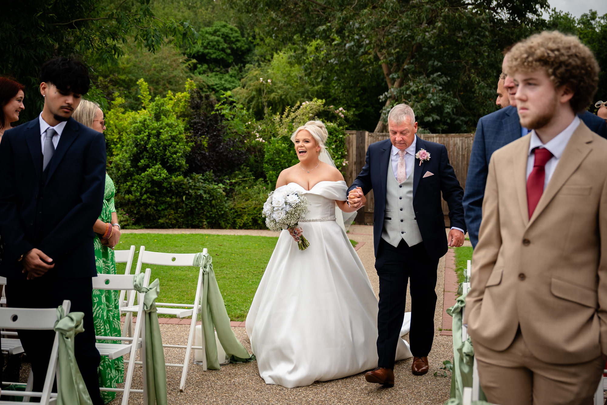 The bride and her father walking past guests towards the outdoor ceremony structure at Hanbury Barns.