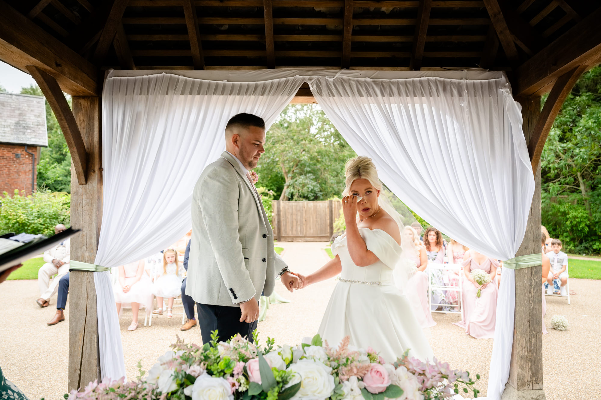 A wide shot showing the bride and groom smiling and laughing during the ceremony in the outdoor gazebo at Hanbury Barns.