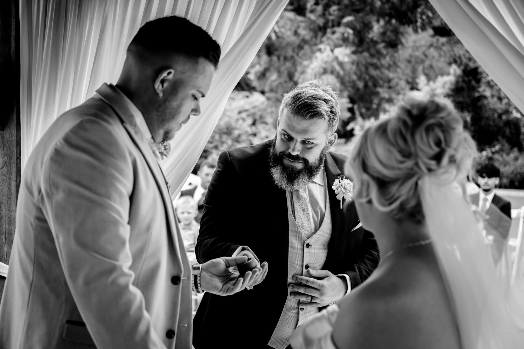 A Hanbury Barns wedding black and white photo of the best man handing the rings to the groom in the middle of the ceremony.