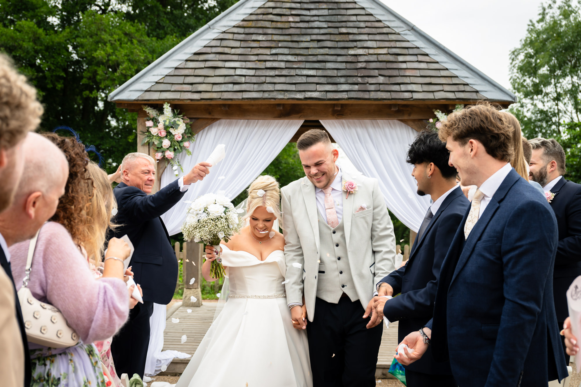 The newly married couple walking back up the aisle, beaming with joy as guests clap and cheer at Hanbury Barns.