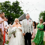 A wedding day at Hanbury Barns group shot of the beaming bride and groom exiting the ceremony surrounded by congratulating guests.