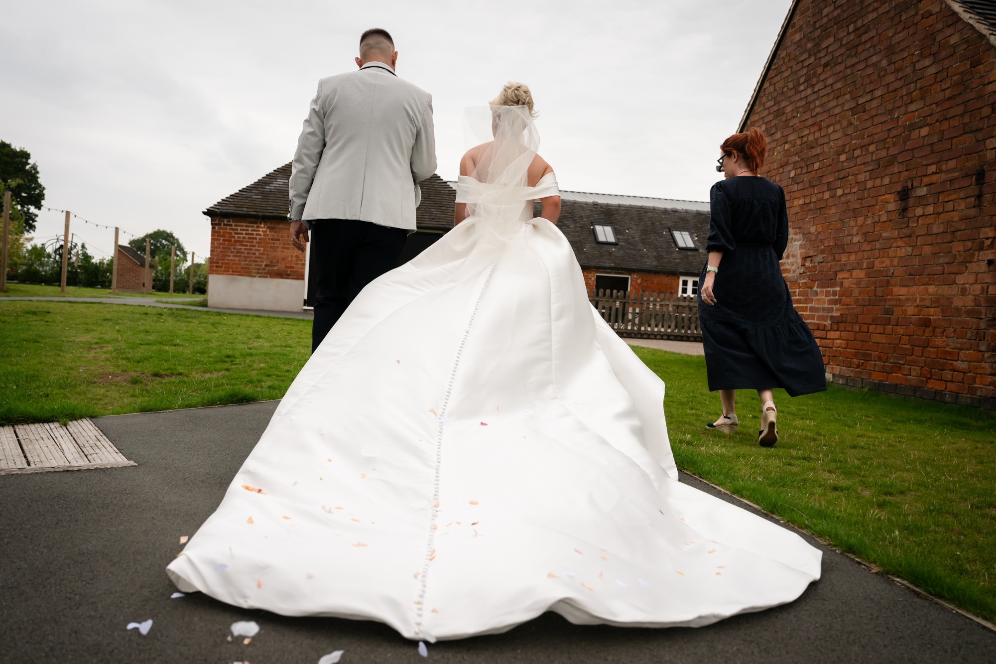 A beautiful view from behind the newly married couple as they walk away from the ceremony area, showing the voluminous train of the bride's dress at Hanbury Barns.
