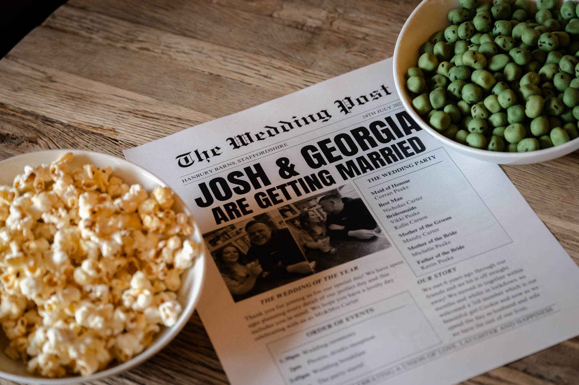 A close-up detail shot of a custom wedding newspaper titled The Wedding Post, featuring the couple’s names, JOSH & GEORGIA, surrounded by bowls of snacks at Hanbury Barns.