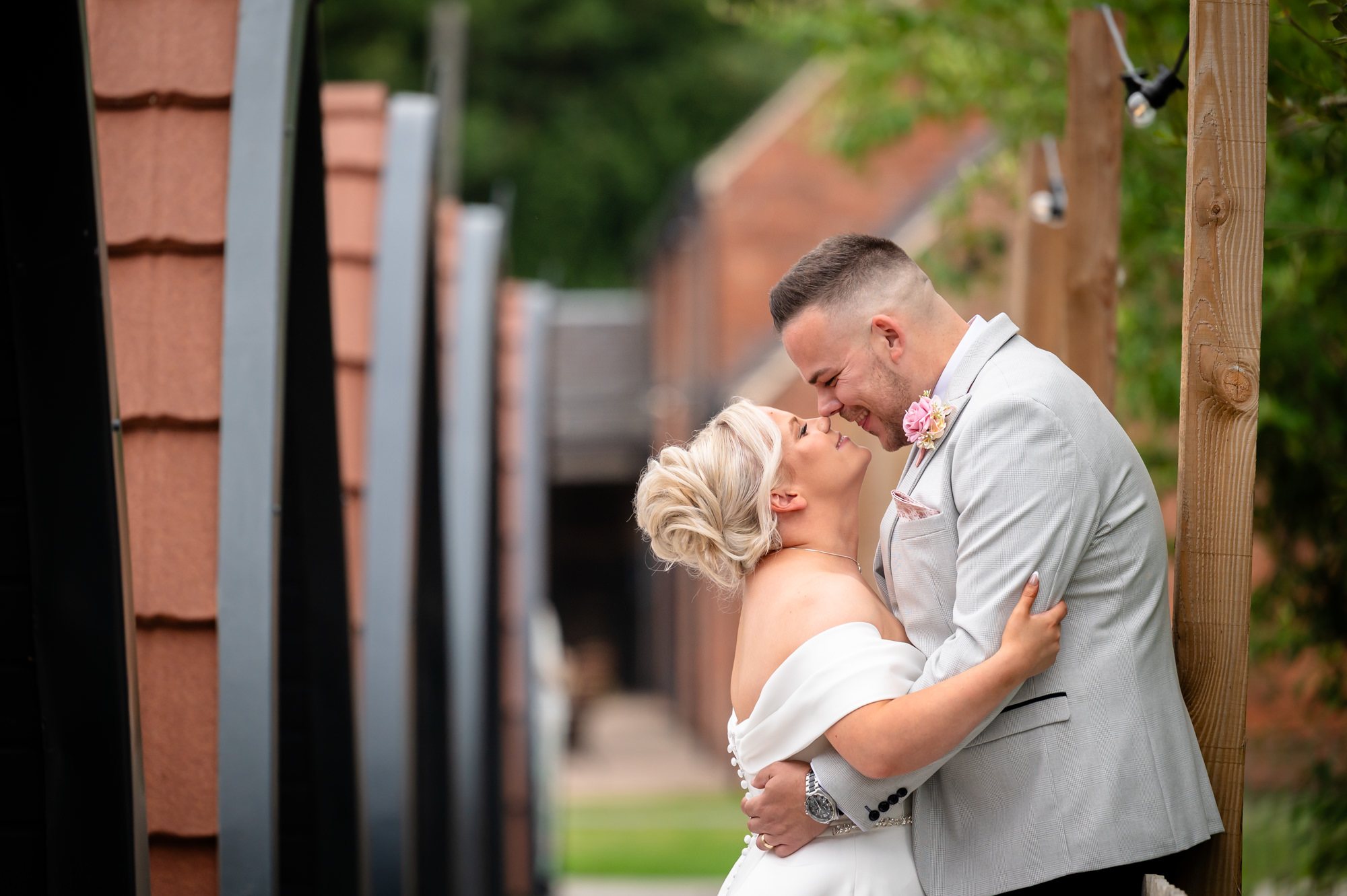 A close-up, romantic outdoor portrait of the groom gently kissing the bride’s temple against the backdrop of Hanbury Barns’ rustic exterior.