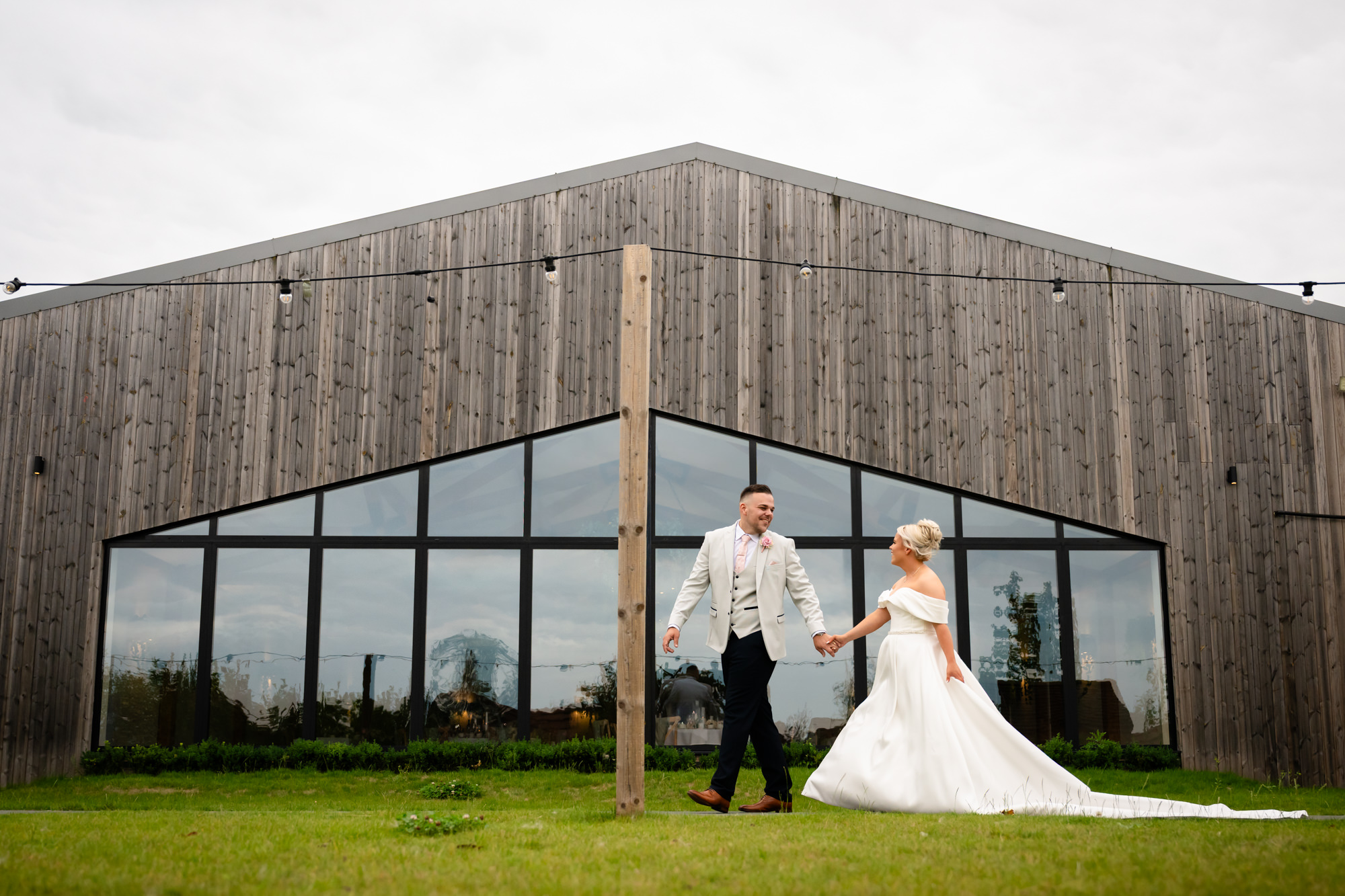 The couple captured in a dramatic long shot against the modern glass front of one of the buildings at Hanbury Barns.