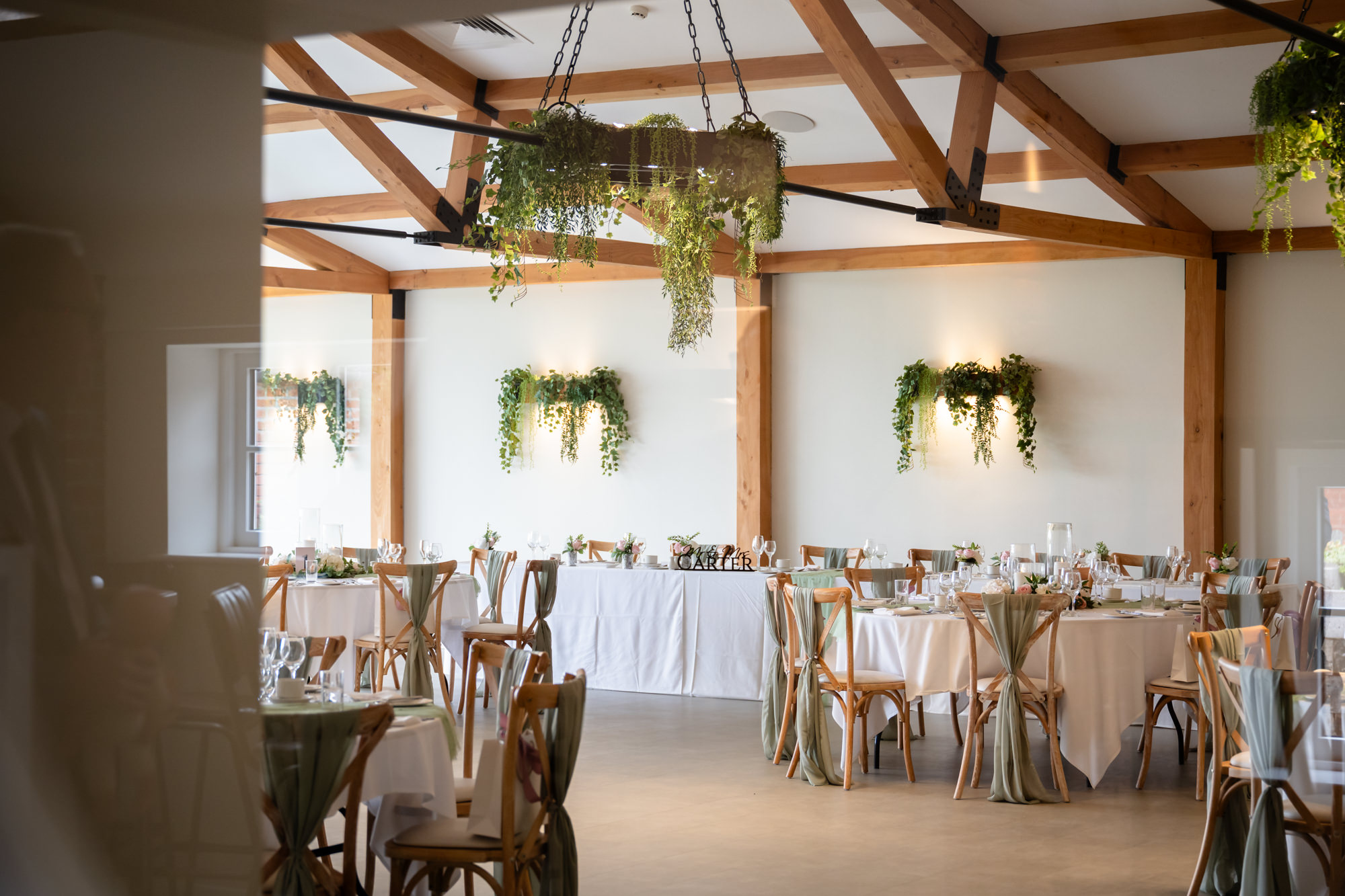 The airy, rustic interior of the Hanbury Barns reception space set up for the wedding breakfast, featuring wooden beams and elegant table settings.