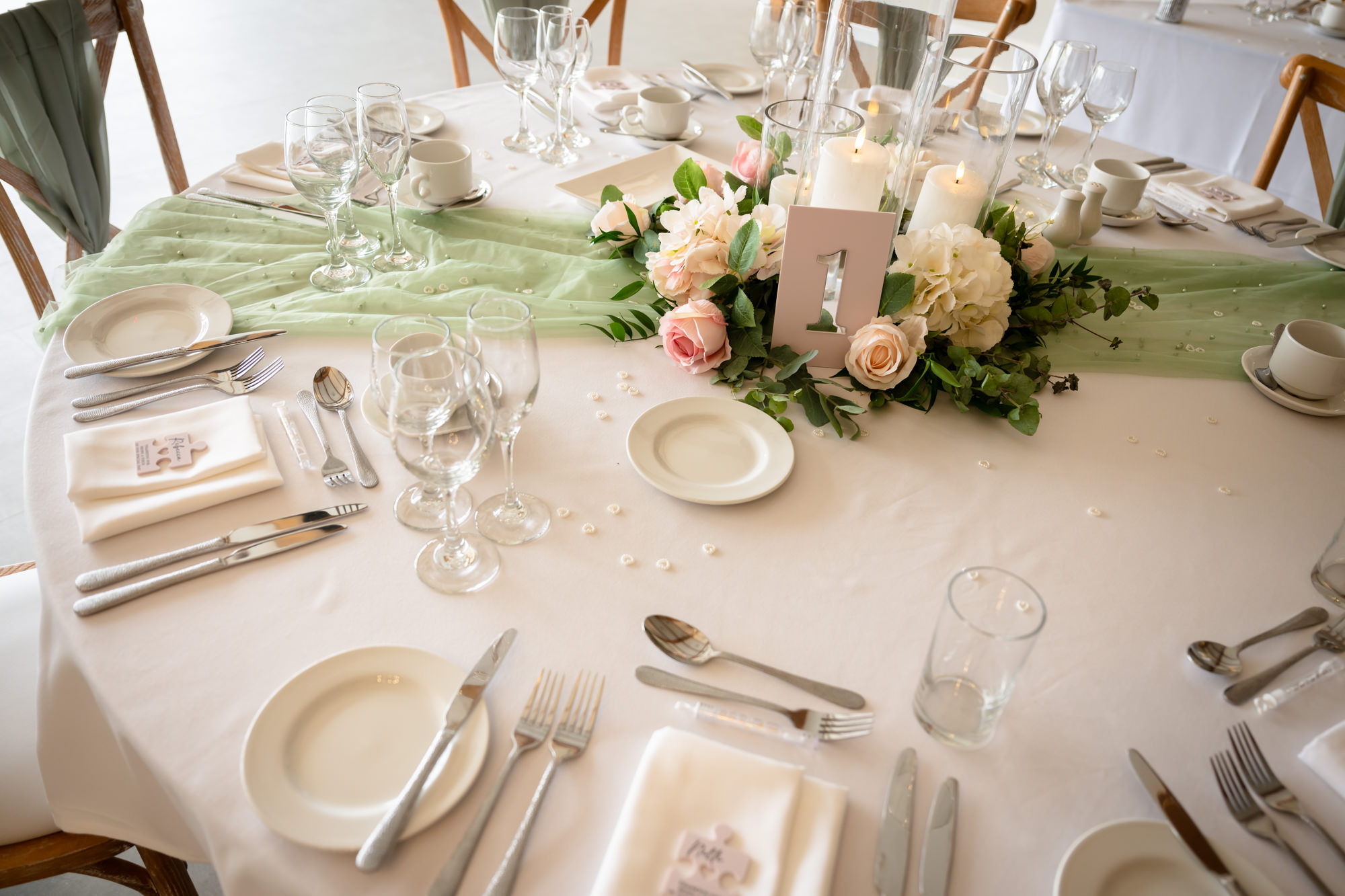 A close-up detail of the clean white table settings, including cutlery and green floral centerpieces at Hanbury Barns.