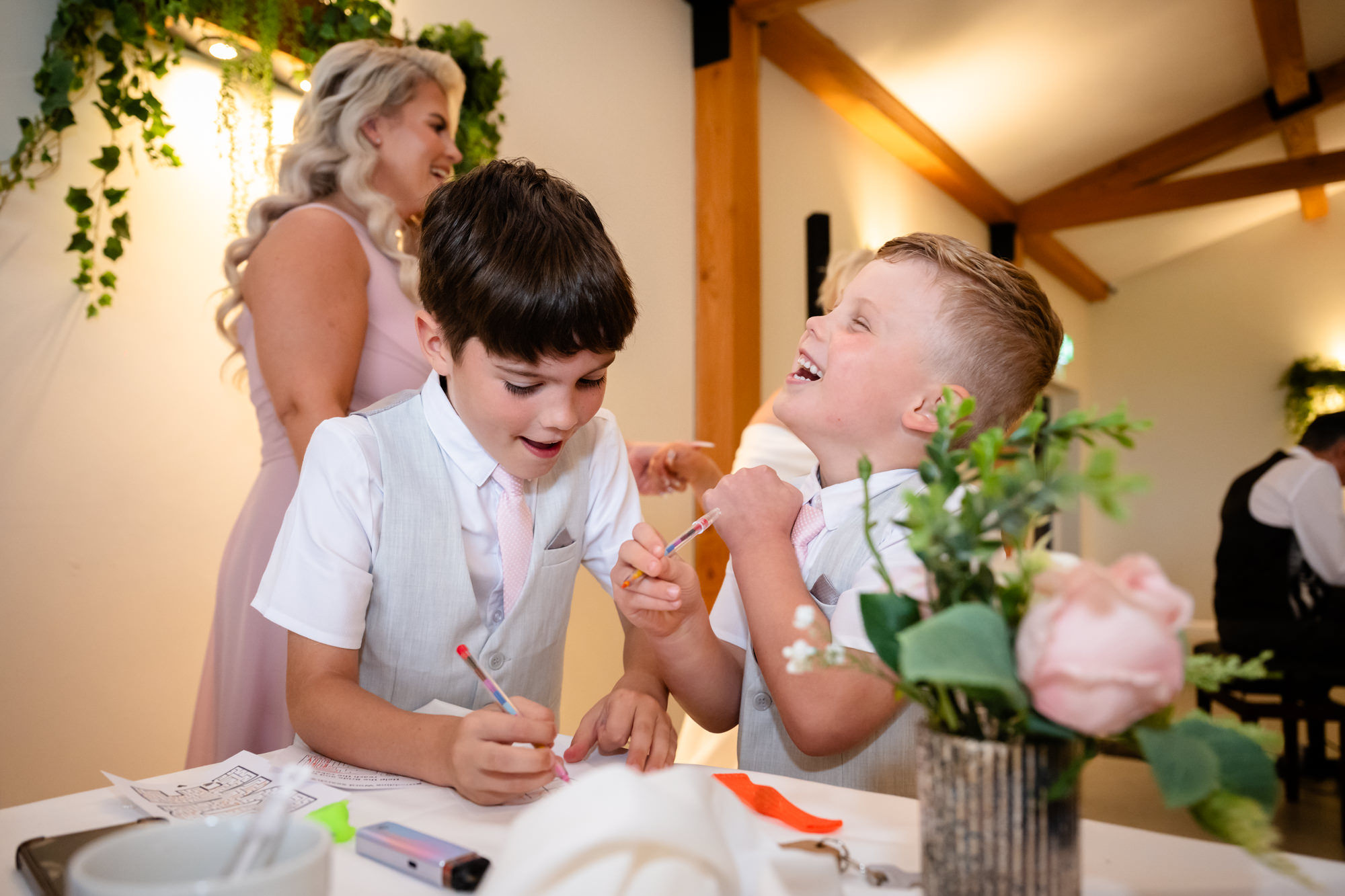 Two young boys sitting and drawing or coloring at one of the tables in the warmly lit Hanbury Barns reception space.