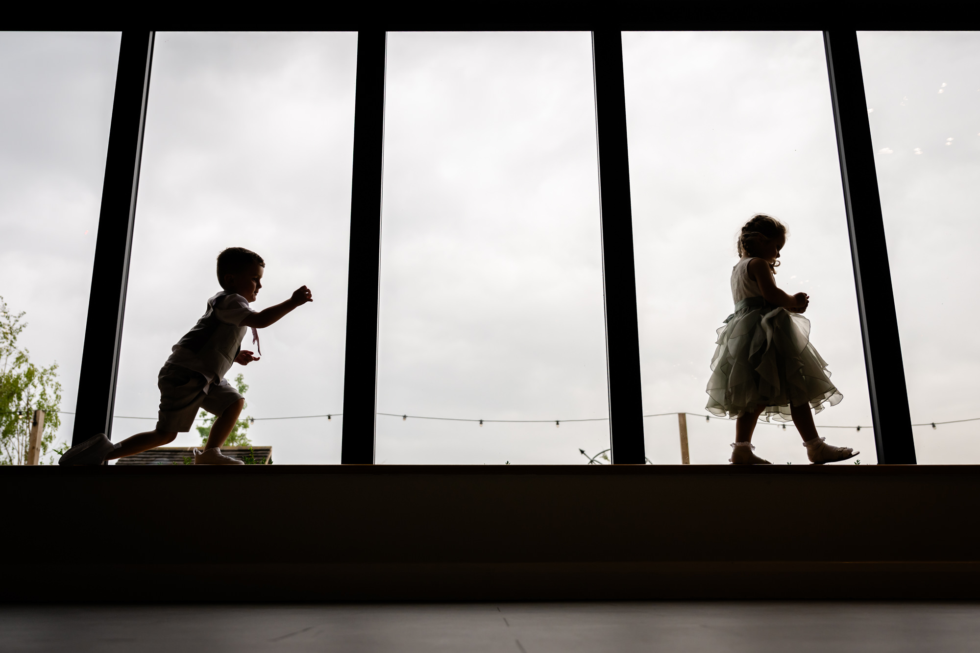 A beautiful moment at Hanbury Barns wedding where the silhouettes of a flower girl and ring bearer are captured playing against a large window.