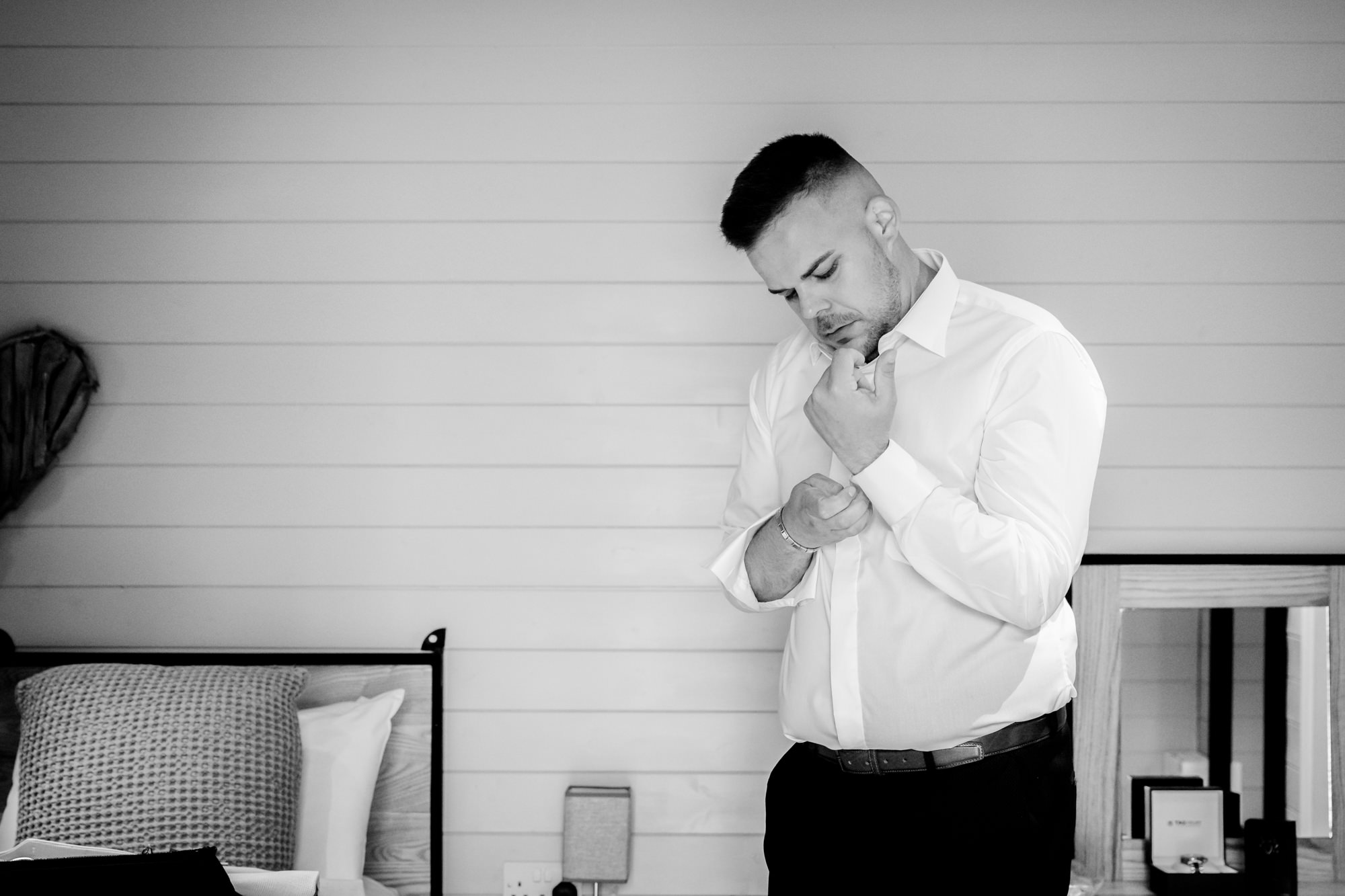 Black and white photo of the groom looking down and adjusting his cufflink in one of the private preparation pods at Hanbury Barns.