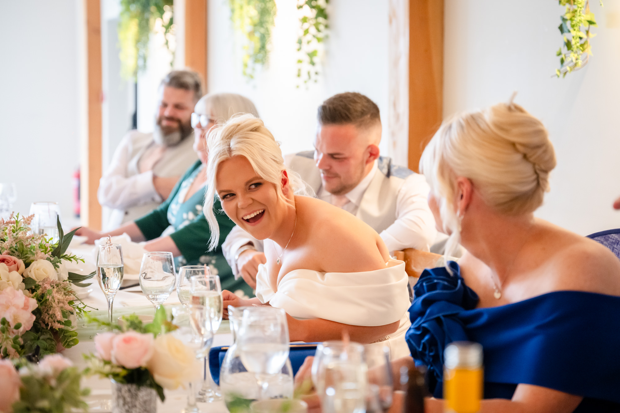The bride and groom smiling and enjoying the speeches at the head table in the beautifully decorated Hanbury Barns reception room.