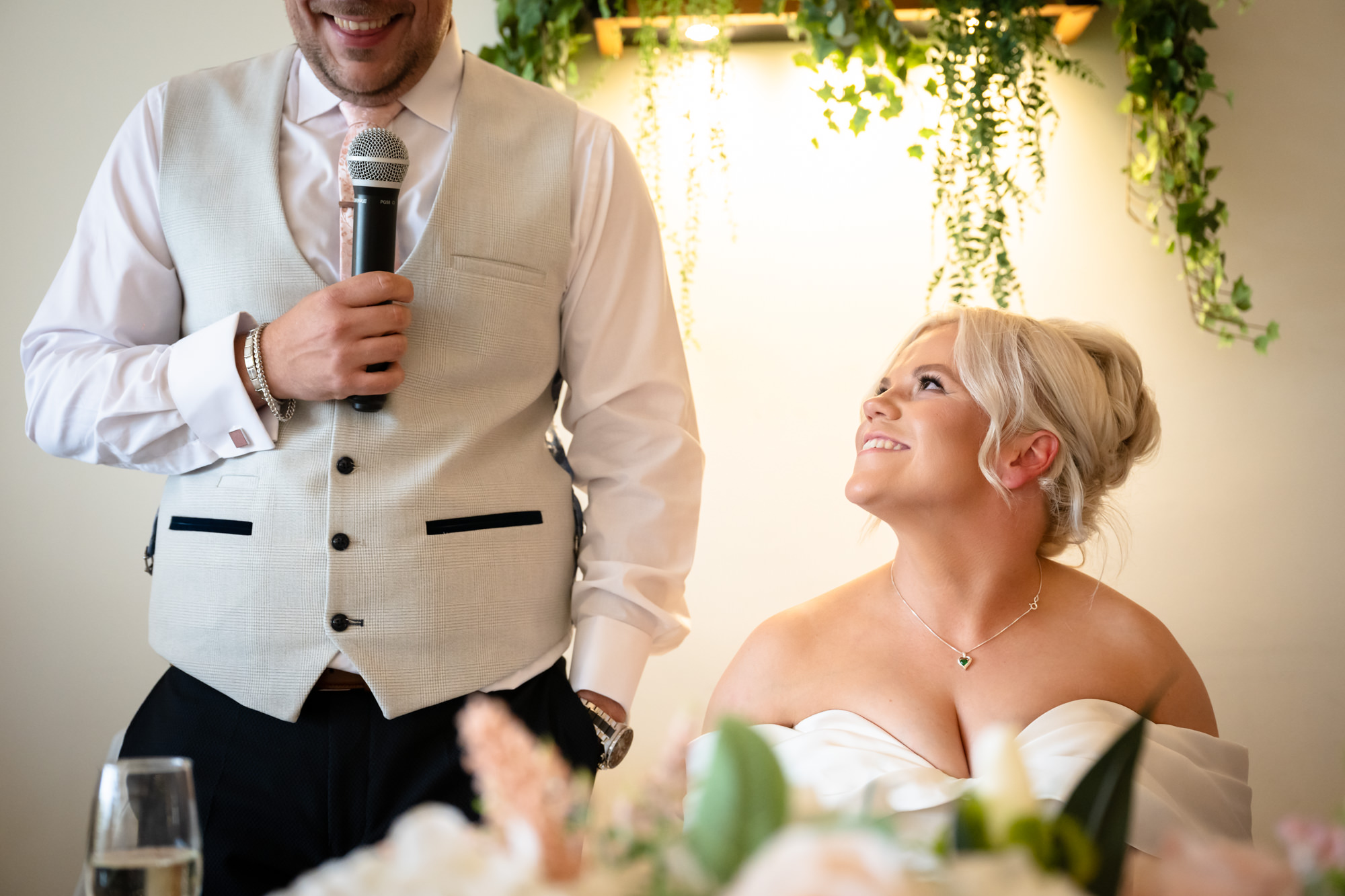 A Hanbury Barns wedding close-up of the groom speaking into the microphone, with the bride looking up at him with love.