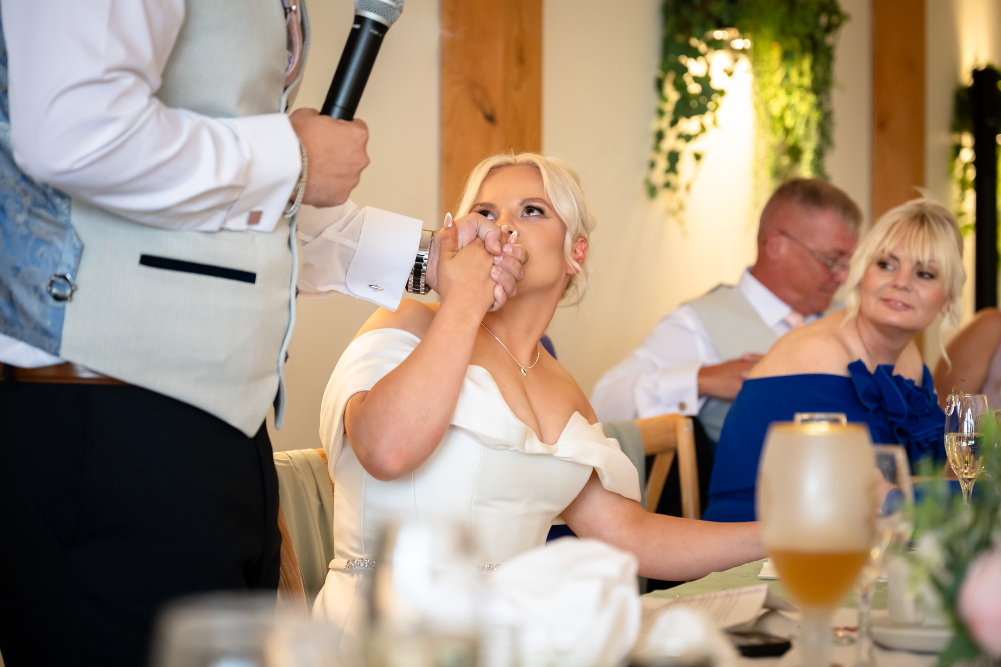 The bride lkissing the groom's hand during a funny or touching speech at Hanbury Barns.
