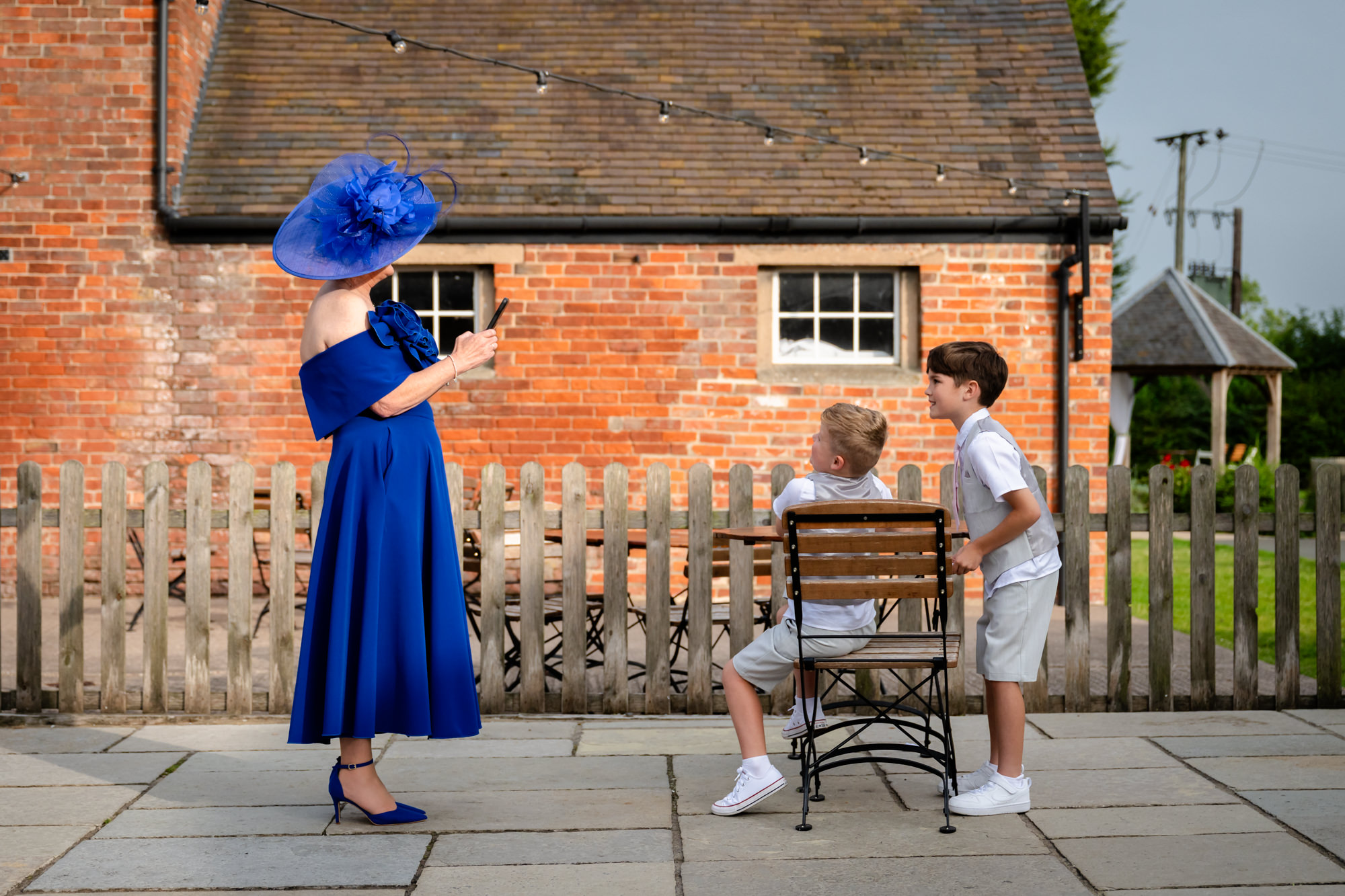 A guest in a bright blue dress taken a photo of two children seated next to the rustic buildings at Hanbury Barns.