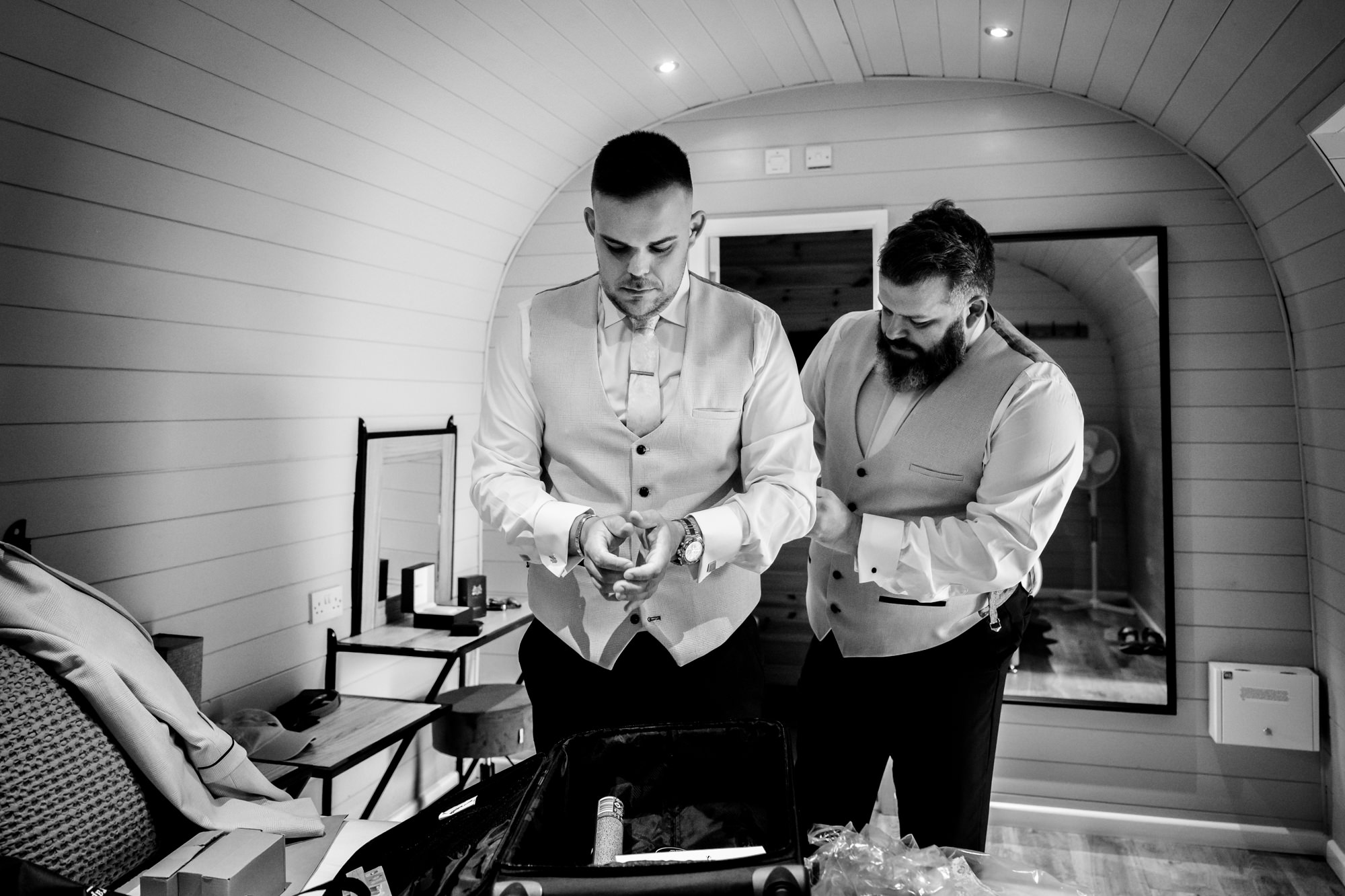 A wedding at Hanbury Barns moment captured showing the groom and his best man adjusting their attire in the small, intimate pod.