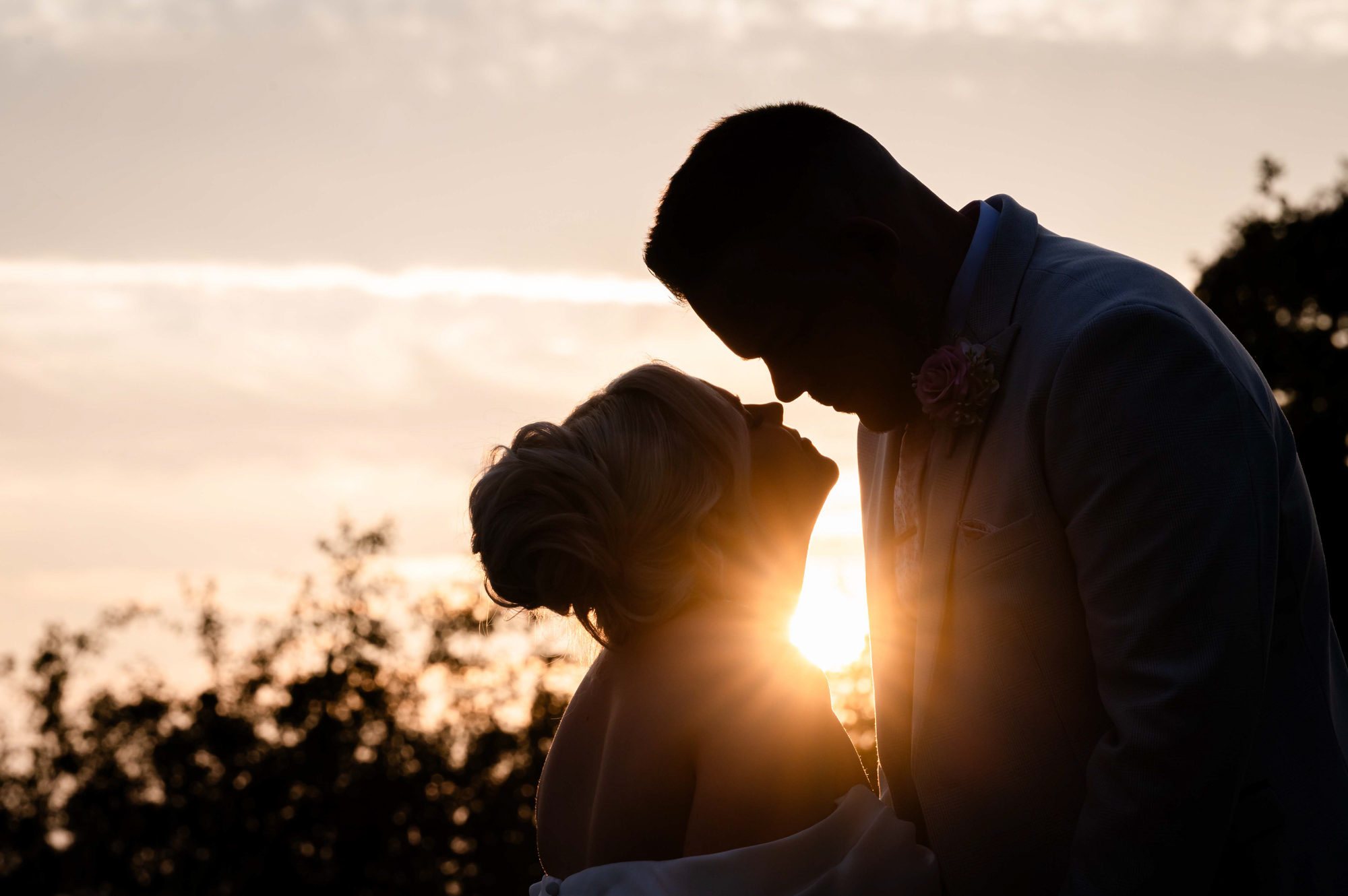 A romantic couple's portrait silhouette of the bride and groom against a dramatic, colorful sunset sky at Hanbury Barns.