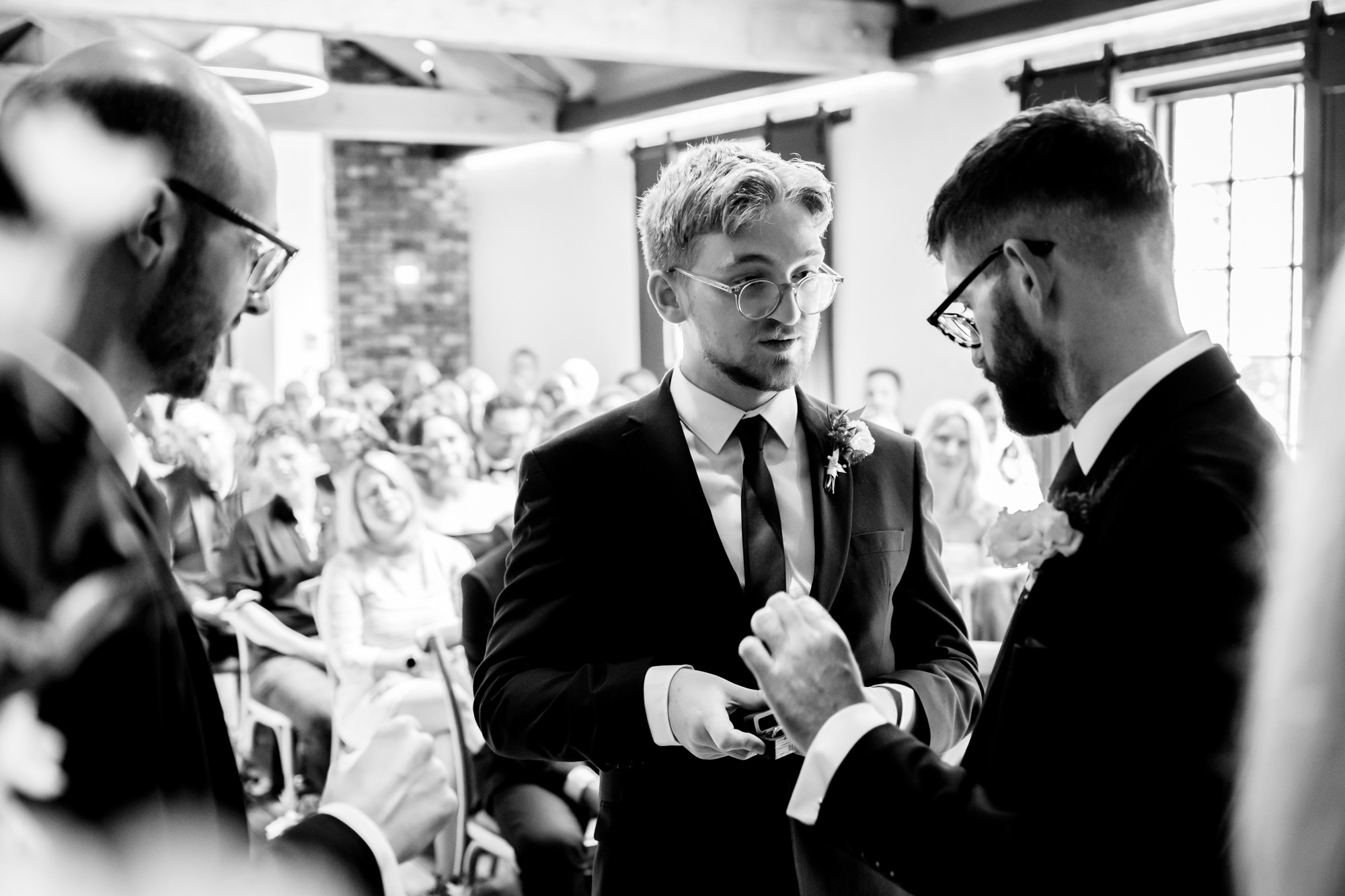 The dark-haired groom and the bald groom share a happy, genuine smile together before the beginning of their marriage ceremony at Castlefield Rooms.