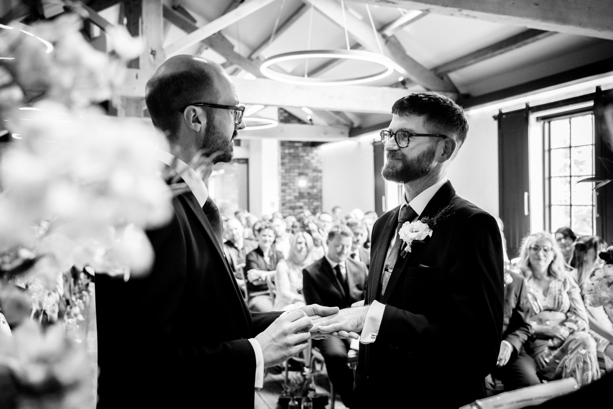 The groom in the green suit and the groom in the blue suit exchange rings during their ceremony at Castlefield Rooms.