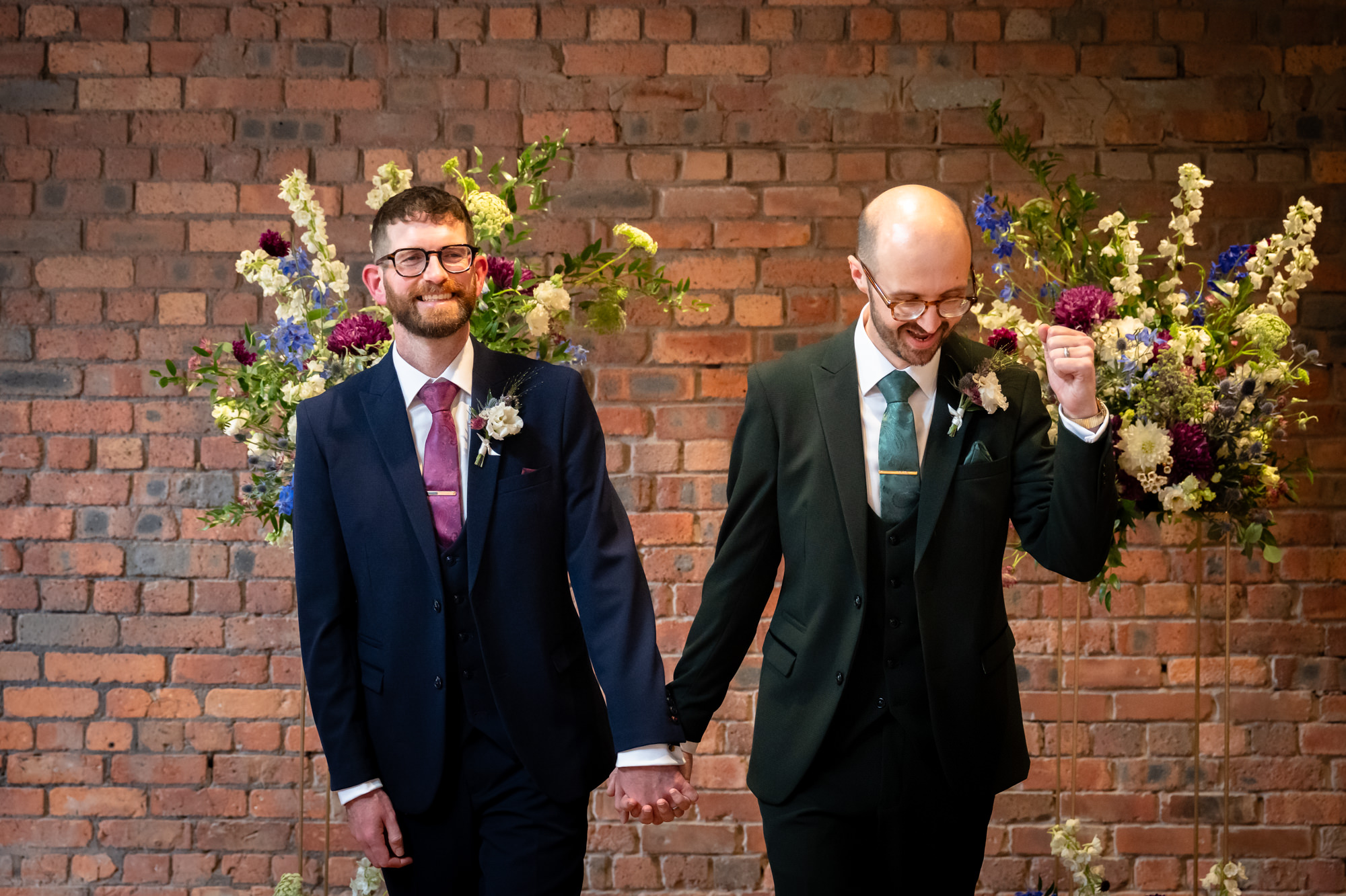 An elevated, wide black and white shot of the two grooms kissing at the end of the aisle during their emotional wedding ceremony at Castlefield Rooms.