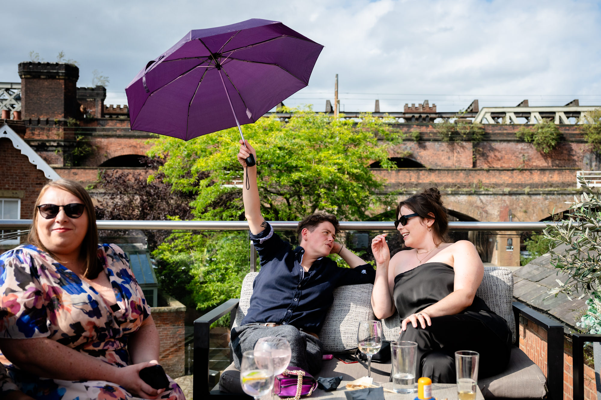 Wedding at Castlefield Rooms. Guests enjoy a glass of champagne during the drinks reception, laughing with delight in the sunshine.