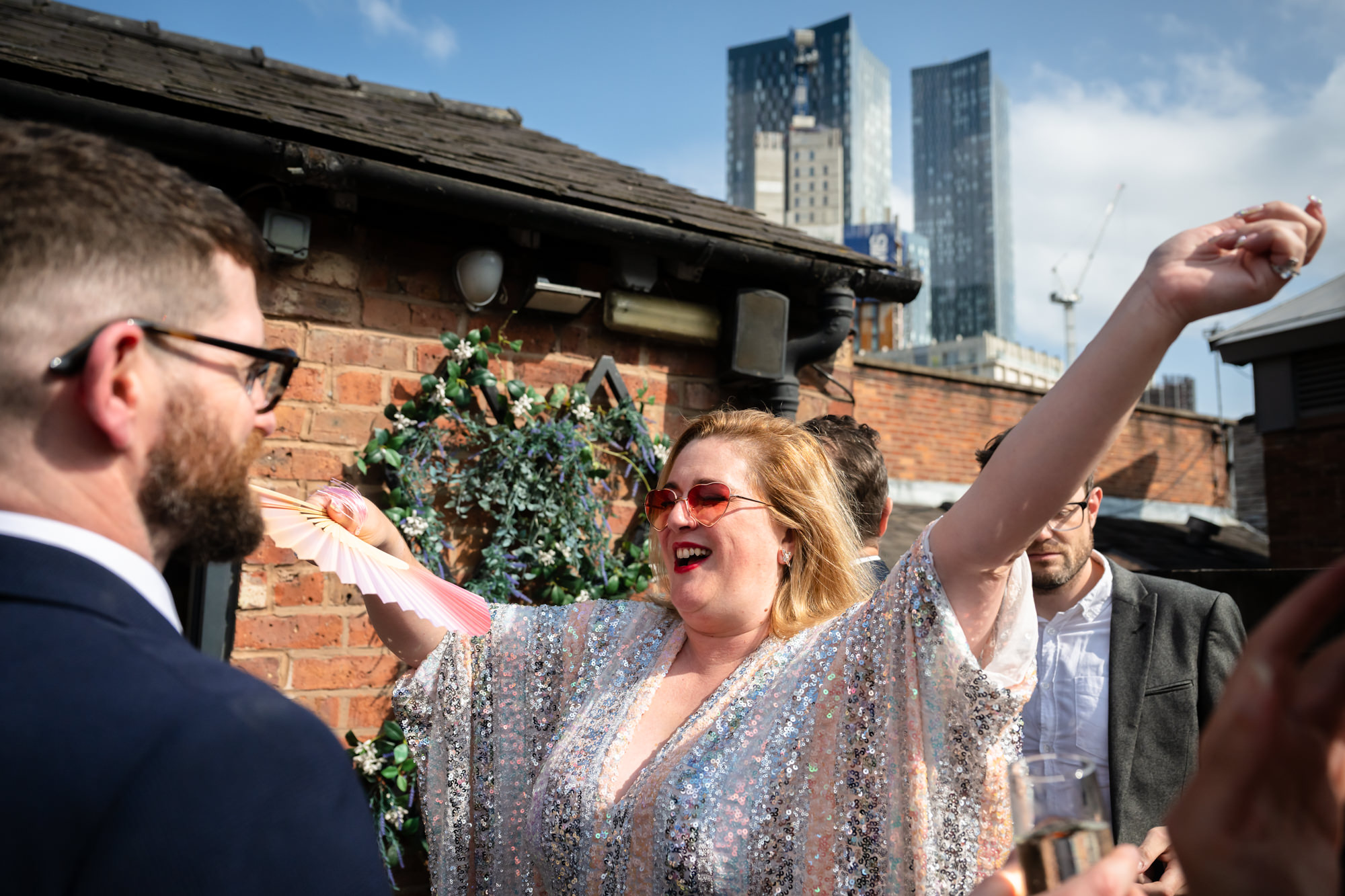 Guests relax and celebrate on the sunny rooftop terrace, raising a glass and holding a purple umbrella at the Castlefield Rooms drinks reception.