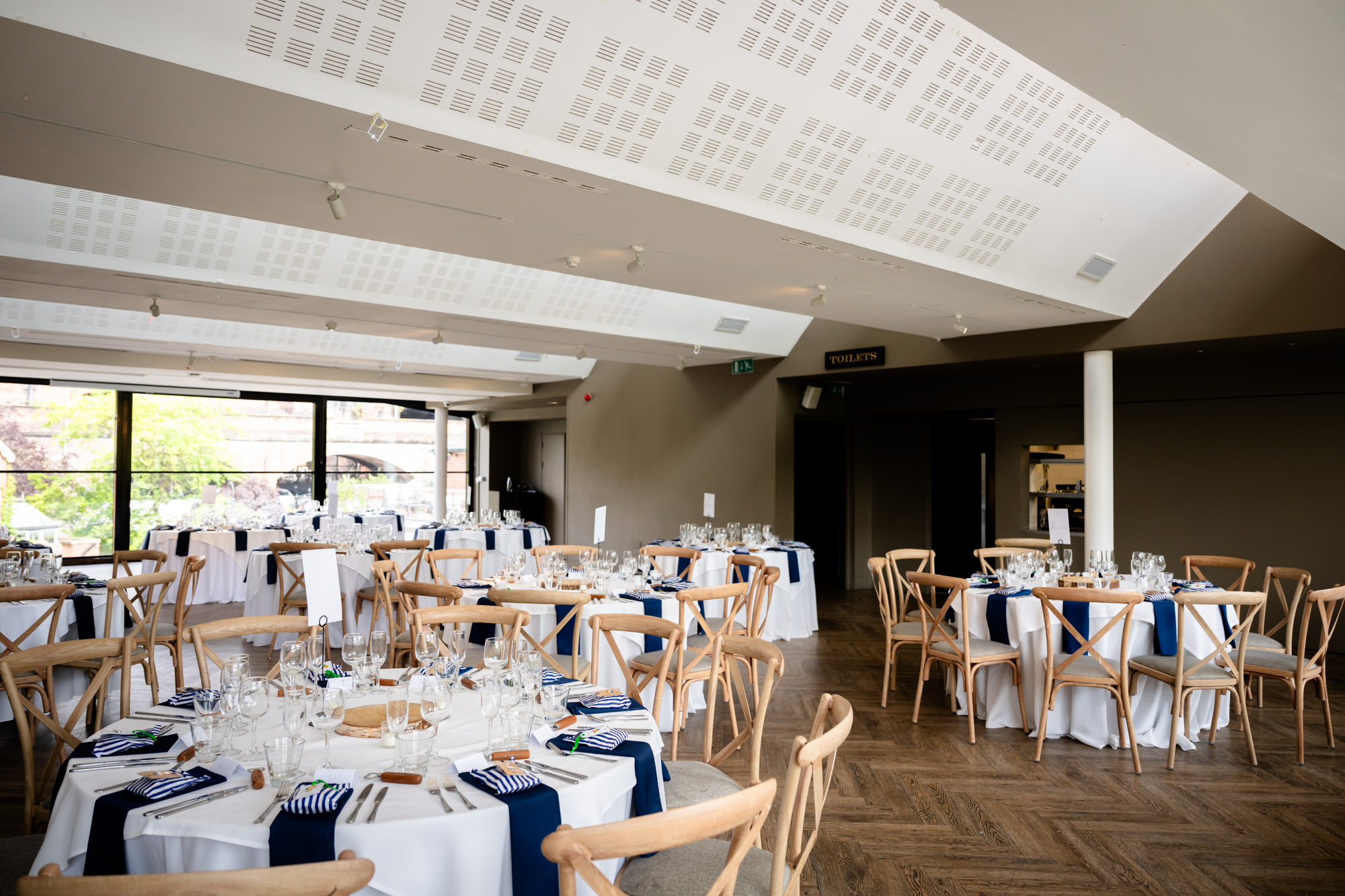 An interior shot showcasing the bright, modern layout of The Merchant room at Castlefield Rooms, set for the wedding breakfast with white linens and wooden chairs.
