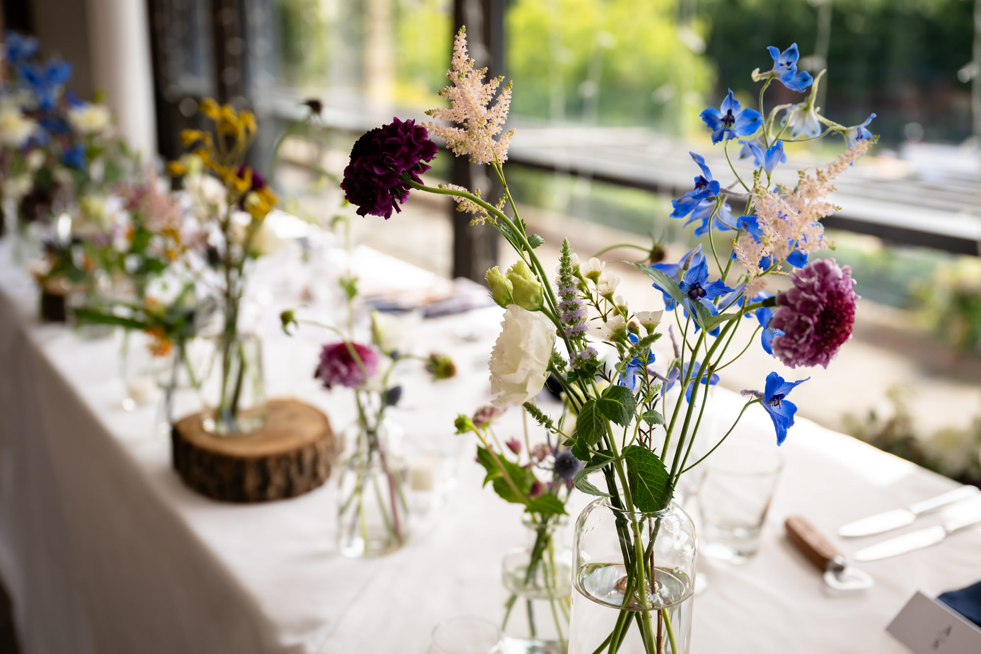 A close-up of a floral centerpiece featuring dark red and blue flowers in a glass vase on one of the wedding breakfast tables at Castlefield Rooms.