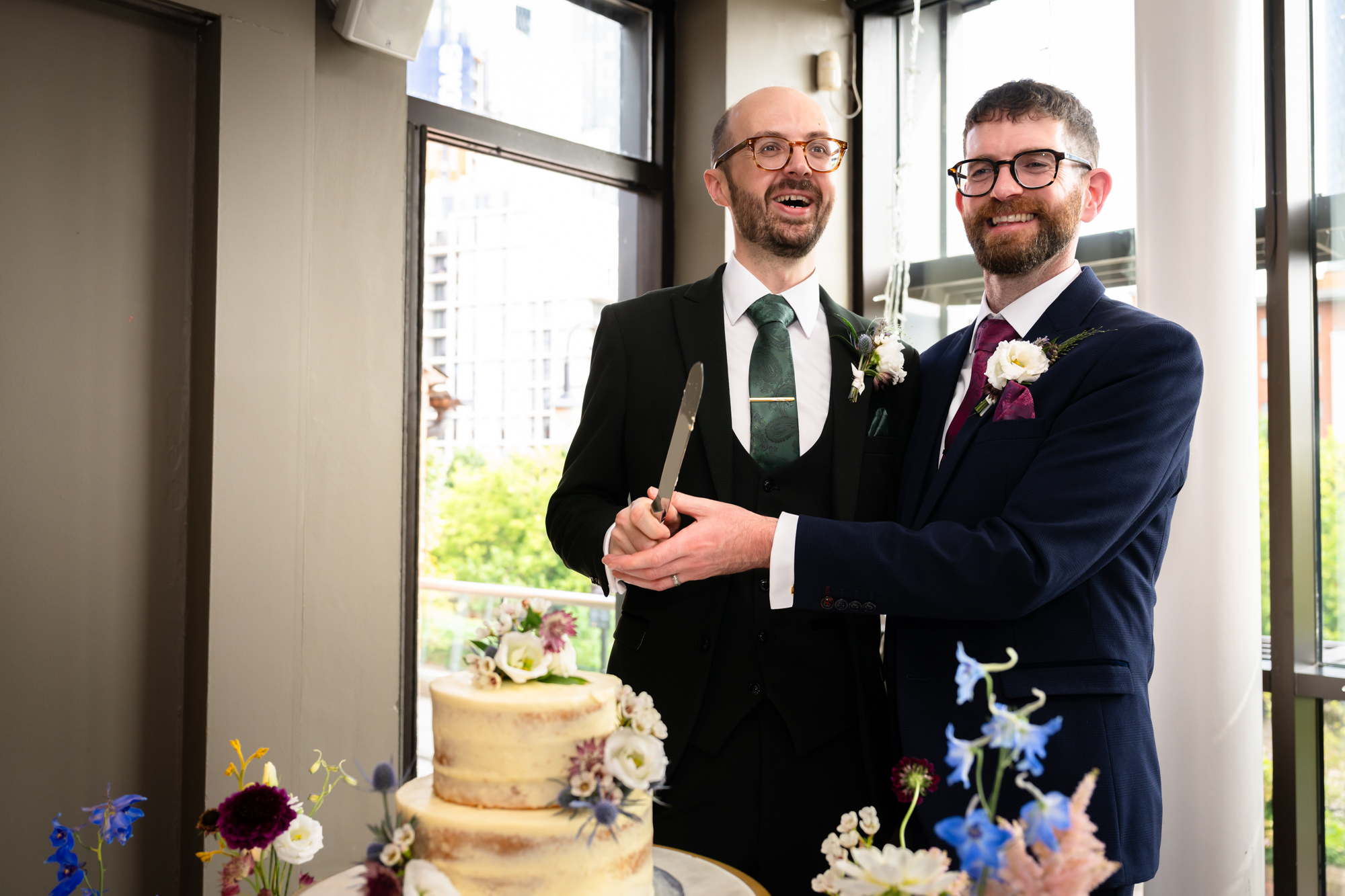 The two grooms raise their hands and cheer as they make their grand entrance into the wedding breakfast reception at Castlefield Rooms.