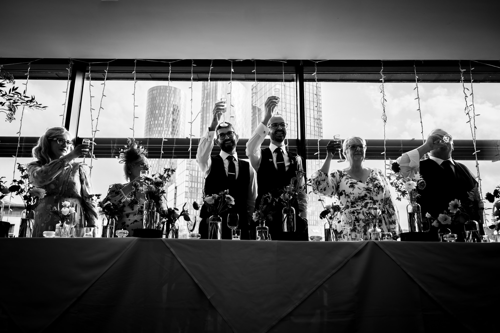 Wedding at Castlefield Rooms. A candid black and white photo of the two grooms sharing a big, unrestrained laugh from the top table during the speeches.