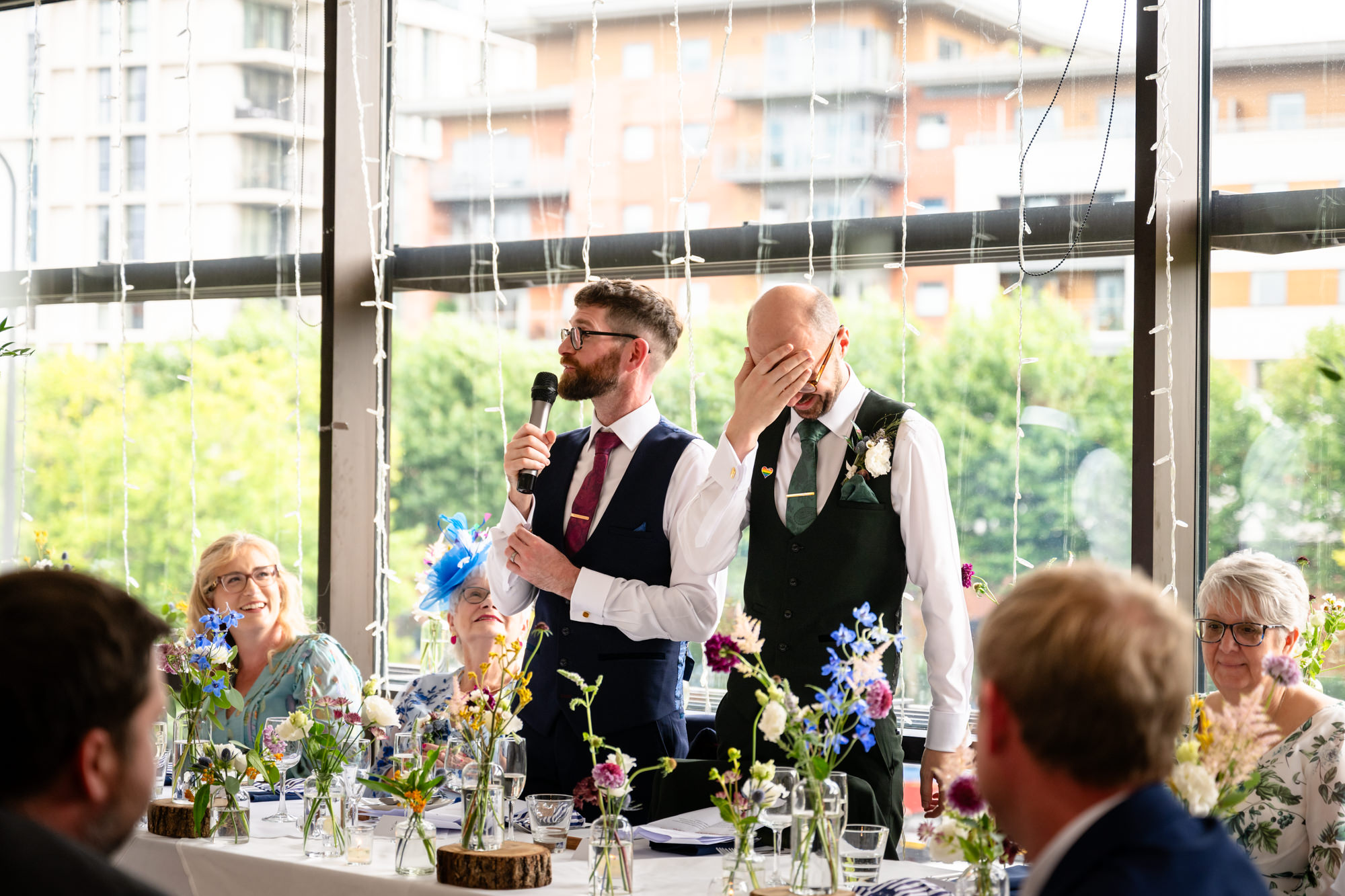 A black and white, wide shot of the grooms and their guests seated at the top table, enjoying the speeches overlooking the city at Castlefield Rooms.