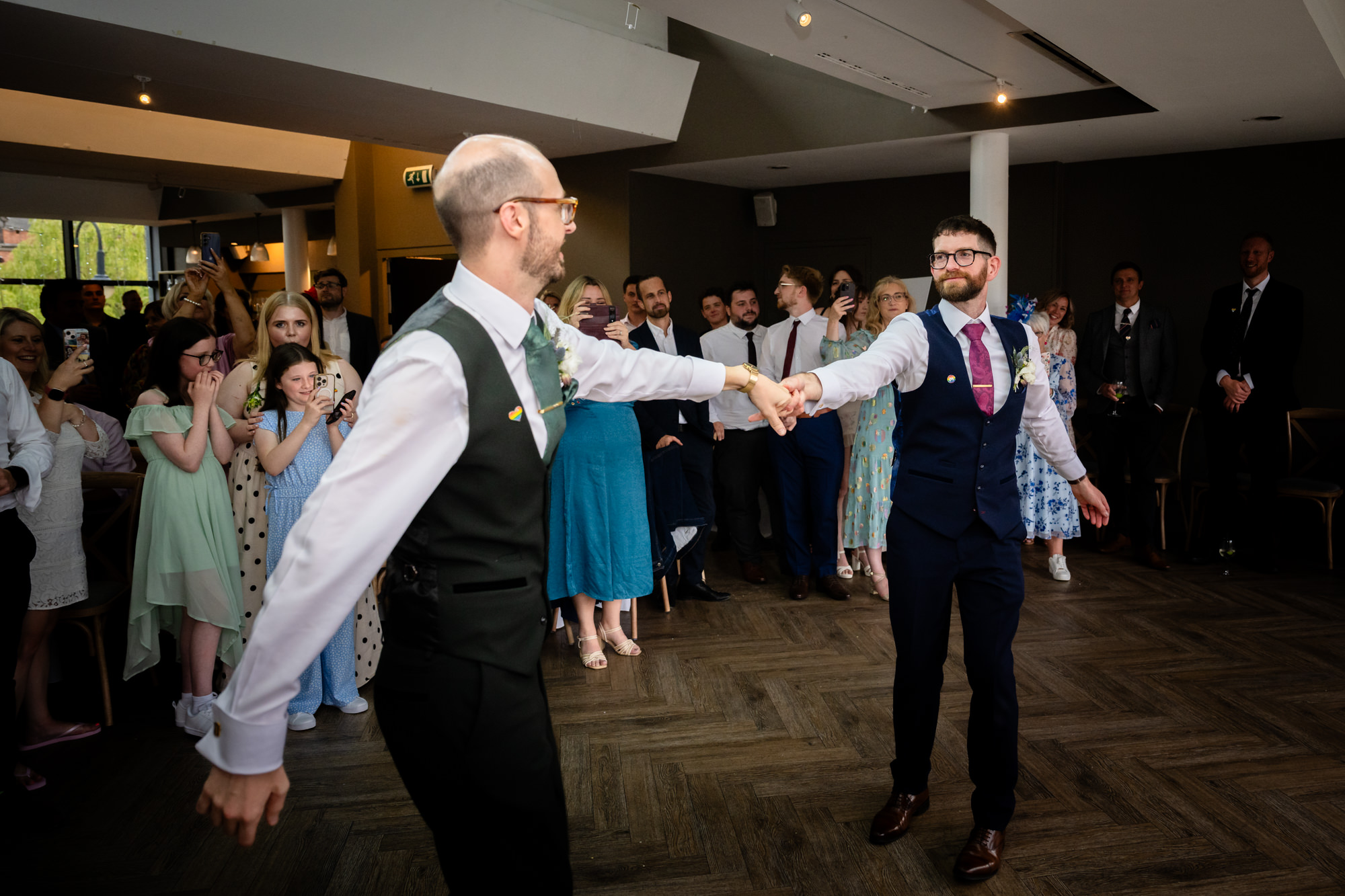 The two grooms take to the dance floor for their first dance, with the groom in the green suit spinning his partner in a romantic and joyful move at Castlefield Rooms.