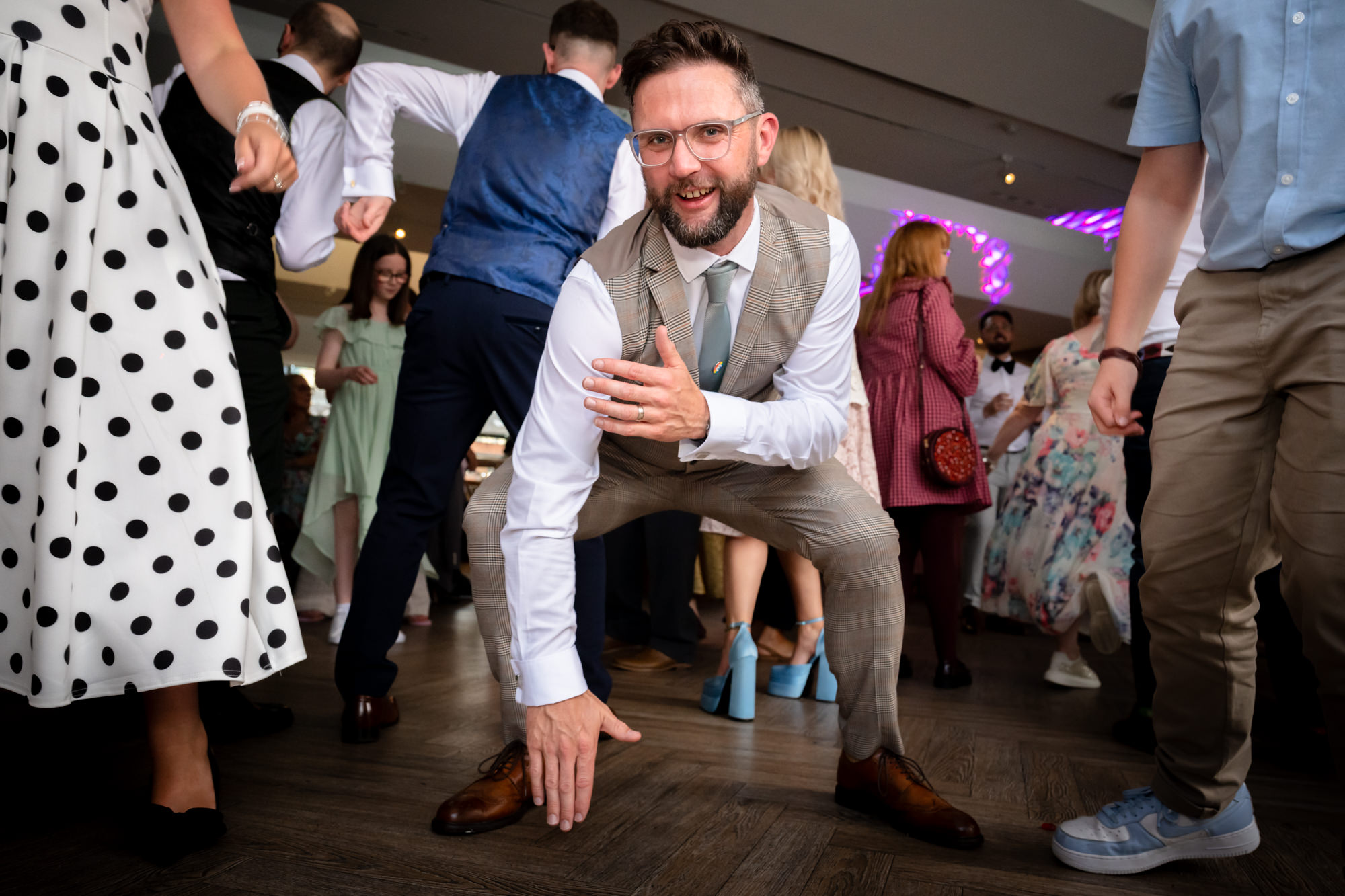 The groom in the green suit twirls a guest on the dance floor during the party, both laughing as they move to the music at the Castlefield Rooms wedding.